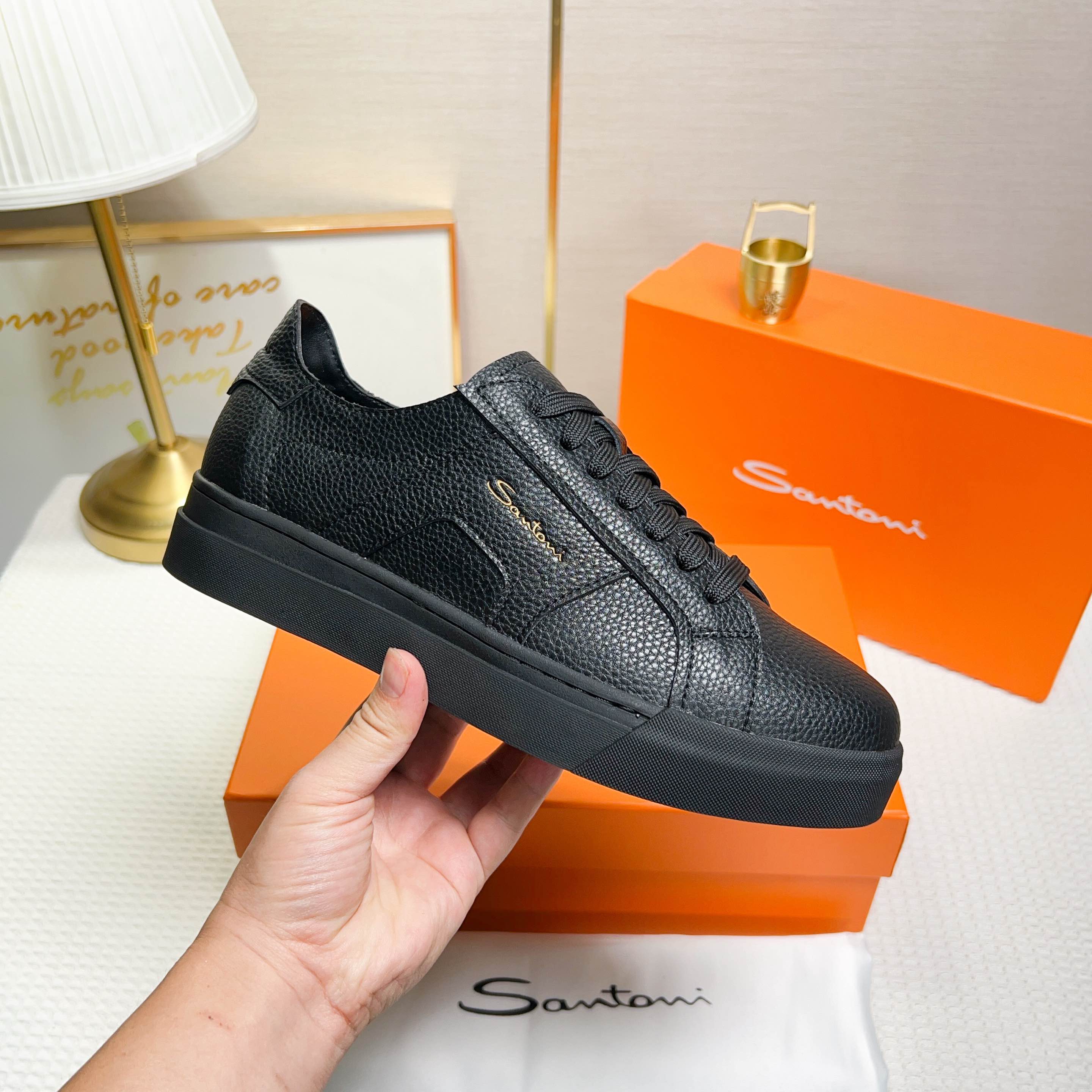 NO:272322,Santoni is a men's low-top sneaker made in Italy. The material and structure are made of lychee-shaped leather, unlined and deconstructed, giving a simple style. The color and details are black, with leather brand logo on the tongue and heel, and the sides are inspired by double buckles to add a sense of fashion. The wear is lace-up design, which is convenient for adjusting the tightness and ensuring a comfortable fit. The sole features rubber cup sole, which is wear-resistant and has strong grip, with Santoni letters printed on the bottom, highlighting the brand identity. This sneaker combines fashion and practicality, suitable for daily casual wear. Size 38-44 (customized for 45),, sneakers19860909Santoni(圣东尼) 这是一款男士低帮运动鞋,由意大利制造. 材质与构造采用荔枝纹皮革制作,未加内衬且解 构设计,呈现简约风格. 颜色与细节鞋身为黑色,鞋舌和鞋跟处饰有 皮革品牌标识,侧边则以双扣环为灵感设计的皮 革细节,增添时尚感. 穿着方式采用系带设计,方便调整松紧度, 确保舒适贴合. 鞋底特色橡胶杯型鞋底,耐磨且抓地力强, 底部印有Santoni字母,彰显品牌身份. 这款运动鞋融合了时尚与实用,适合日常休闲穿 着. 38-44码（45定做）,,sneakers,Men's shoes