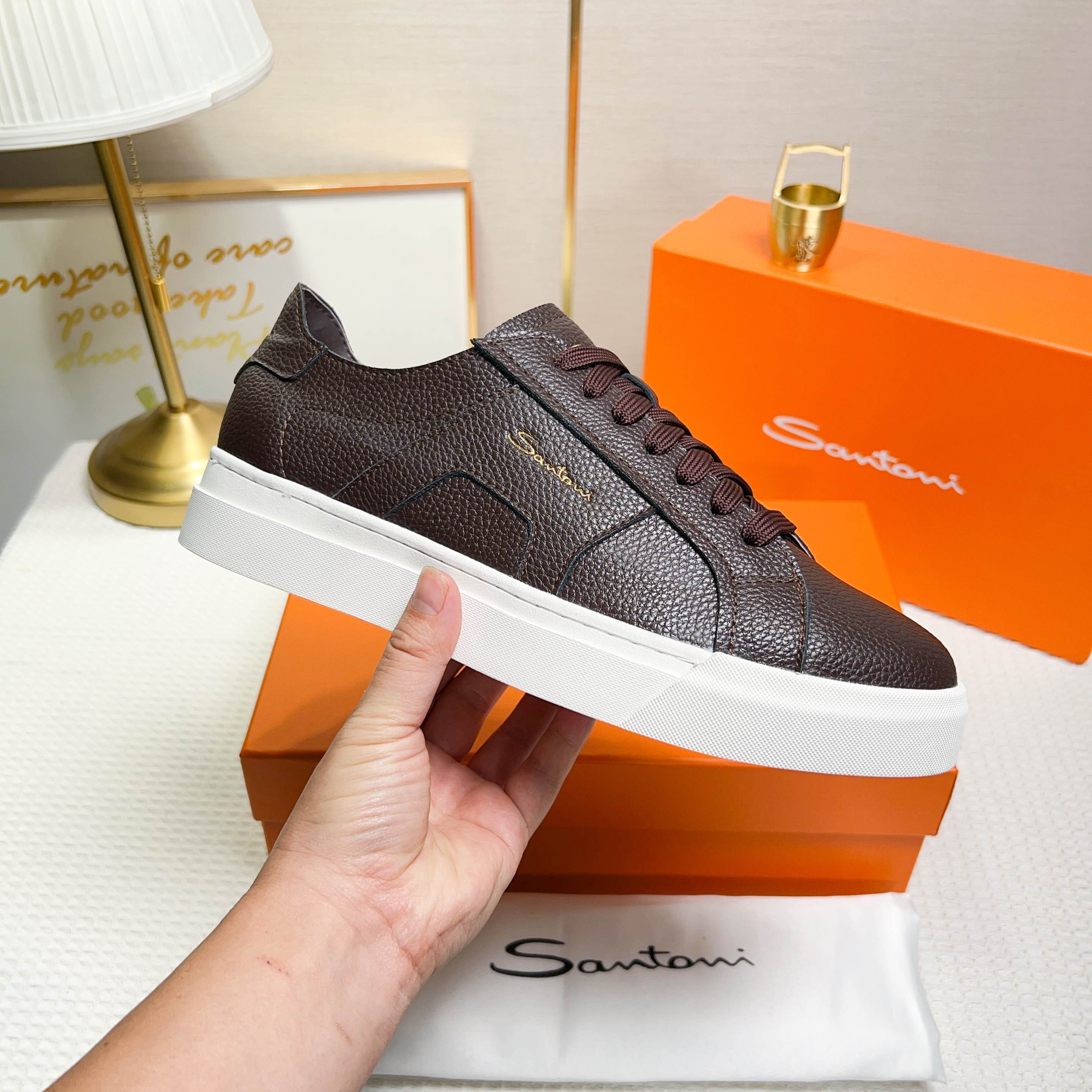 NO:272328,Santoni is a men's low-top sneaker made in Italy. The material and structure are made of lychee-shaped leather, unlined and deconstructed, giving a simple style. The color and details are brown, with leather brand logo on the tongue and heel, and the sides are inspired by double buckles to add a sense of fashion. The wear is lace-up design, which is convenient for adjusting the tightness and ensuring a comfortable fit. The sole features rubber cup sole, which is wear-resistant and has strong grip, and the Santoni letters are printed on the bottom, highlighting the brand identity. This sneaker combines fashion and practicality, suitable for daily casual wear. Size 38-44 (customized for 45),, sneakers19860909Santoni(圣东尼) 这是一款男士低帮运动鞋,由意大利制造. 材质与构造采用荔枝纹皮革制作,未加内衬且解 构设计,呈现简约风格. 颜色与细节鞋身为咖色,鞋舌和鞋跟处饰有 皮革品牌标识,侧边则以双扣环为灵感设计的皮 革细节,增添时尚感. 穿着方式采用系带设计,方便调整松紧度, 确保舒适贴合. 鞋底特色橡胶杯型鞋底,耐磨且抓地力强, 底部印有Santoni字母,彰显品牌身份. 这款运动鞋融合了时尚与实用,适合日常休闲穿 着. 38-44码（45定做）,,sneakers,Men's shoes