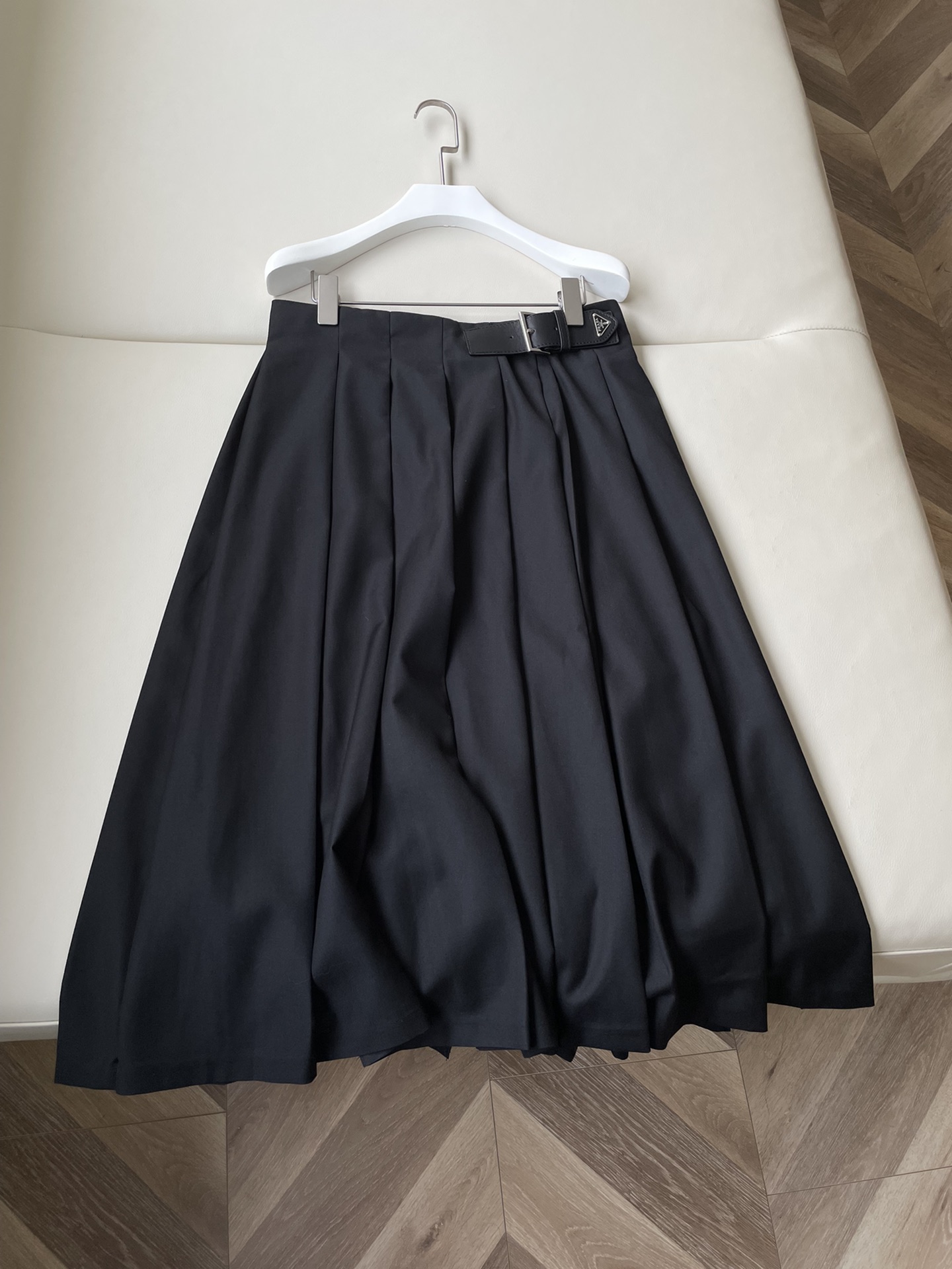 Prada 百褶半裙这款经典的中长半身裙是Prada系列中极具代表性的百褶裙款式，皮革饰带前端带有涂珐琅金属三角形徽标，平添经典意味。采用Re-Nylon材质制成，一种以以海洋中回收的塑料材料制成的环保面料，低腰设计凸显腰线颜色：黑色尺码：36 38 40 42