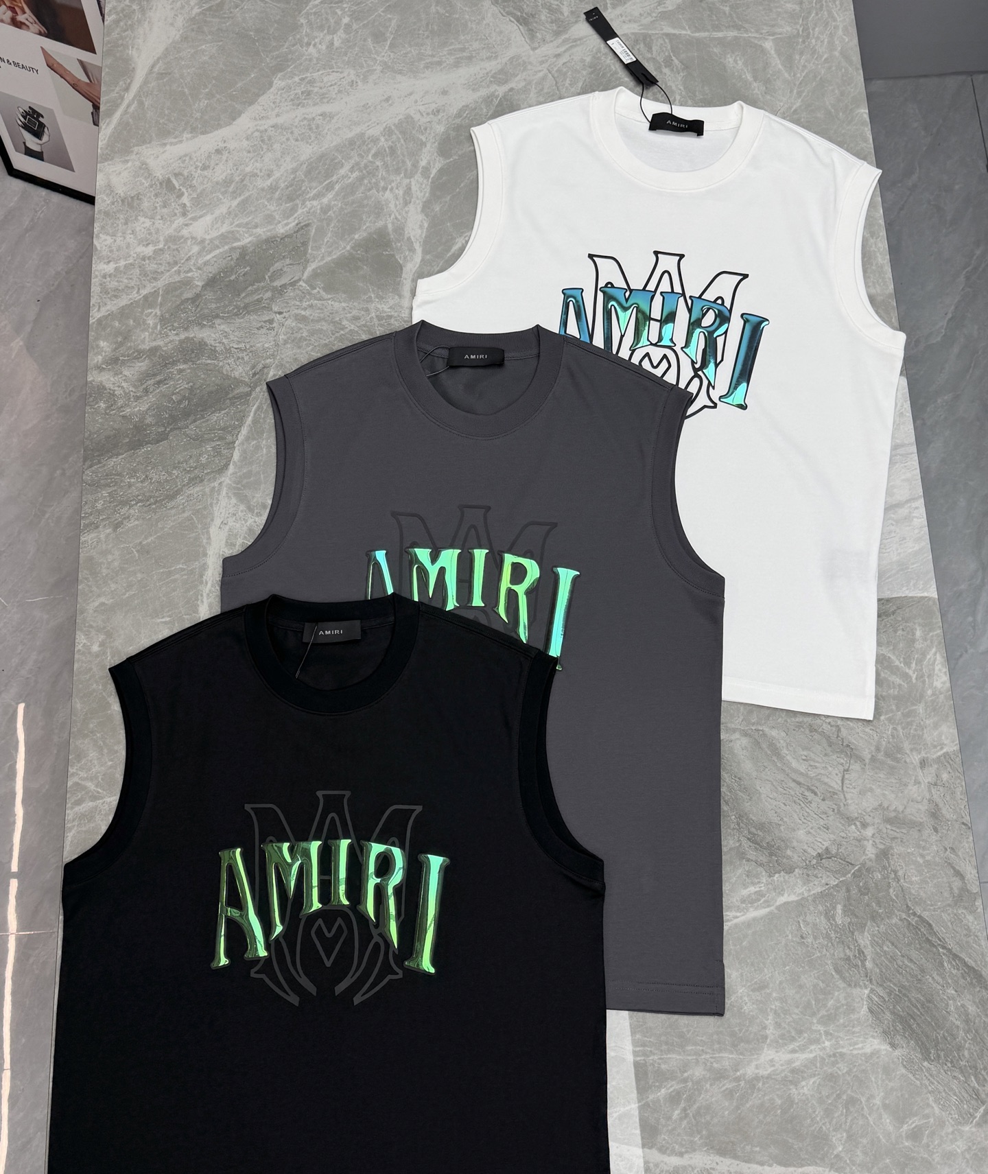 AMIRI无袖印花背心，黑色、灰色、白色三色可选，正面品牌Logo+荧光绿蓝渐变，街头感十足✨。高品质冰