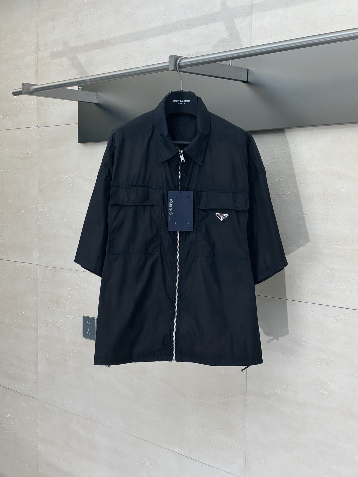 NO:528186,Prad*/Prada nylon double pocket short-sleeved shirt is made of light Re-Nylon environmentally friendly material, combining durability and environmentally friendly concepts. The oversize design presents a modern minimalist style, with square silhouettes and flat bottom edges to show neat lines. The classic lapel design enhances the overall texture, with two practical flip patch pockets on the front, and the zipper opening and closing design adds movement. The details are embellished with the iconic enamel triangular metal logo to highlight the classic characteristics of the brand. The shirt is made of exquisite craftsmanship to ensure that each joint is flat and firm. In order to maintain the characteristics of the fabric and practice the environmentally friendly concept, it is recommended to reduce the cleaning frequency, dry naturally after use, and choose professional environmentally friendly dry cleaning services. The Re-Nylon material is not only light and comfortable, but also achieves sustainable development through regeneration technology, perfectly blending functionality and fashion sense to create an urban item that combines practical and aesthetics.  SizeS/M/L/XL,,prada,prada,versace,shirts,T-shirt,alexander wang19860909Prad*/普拉达 尼龙双口袋短袖衬衫 采用轻盈的Re-Nylon环保材质打造,兼具耐用性与环保理念.oversize版型设计呈现现代极简风格,方正廓形搭配平直底边,展现利落线条.经典翻领设计提升整体质感,正面配备两个实用翻盖贴袋,拉链开合设计增添运动.细节处点缀标志性涂珐琅三角形金属徽标,彰显品牌经典特色.该衬衫采用精湛工艺制作,确保每处接缝平整牢固.为保持面料特性并践行环保理念,建议减少清洗频率,使用后自然晾干,并选择专业环保干洗服务.Re-Nylon材质不仅轻便舒适,更通过再生技术实现可持续发展,完美融合功能性与时尚感,打造兼具实用与美感的都市单品. SizeS/M/L/XL,,prada,prada,versace,shirts,T-shirt,alexander wang,Men's clothing