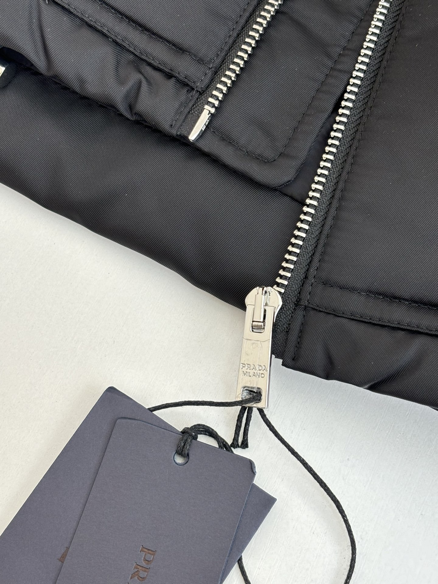 Prad*/普拉达 翻袋倒三角铁牌羽绒外套再生尼龙面料材质，再生尼龙面料也被称为尼龙回料，是一种环保面料