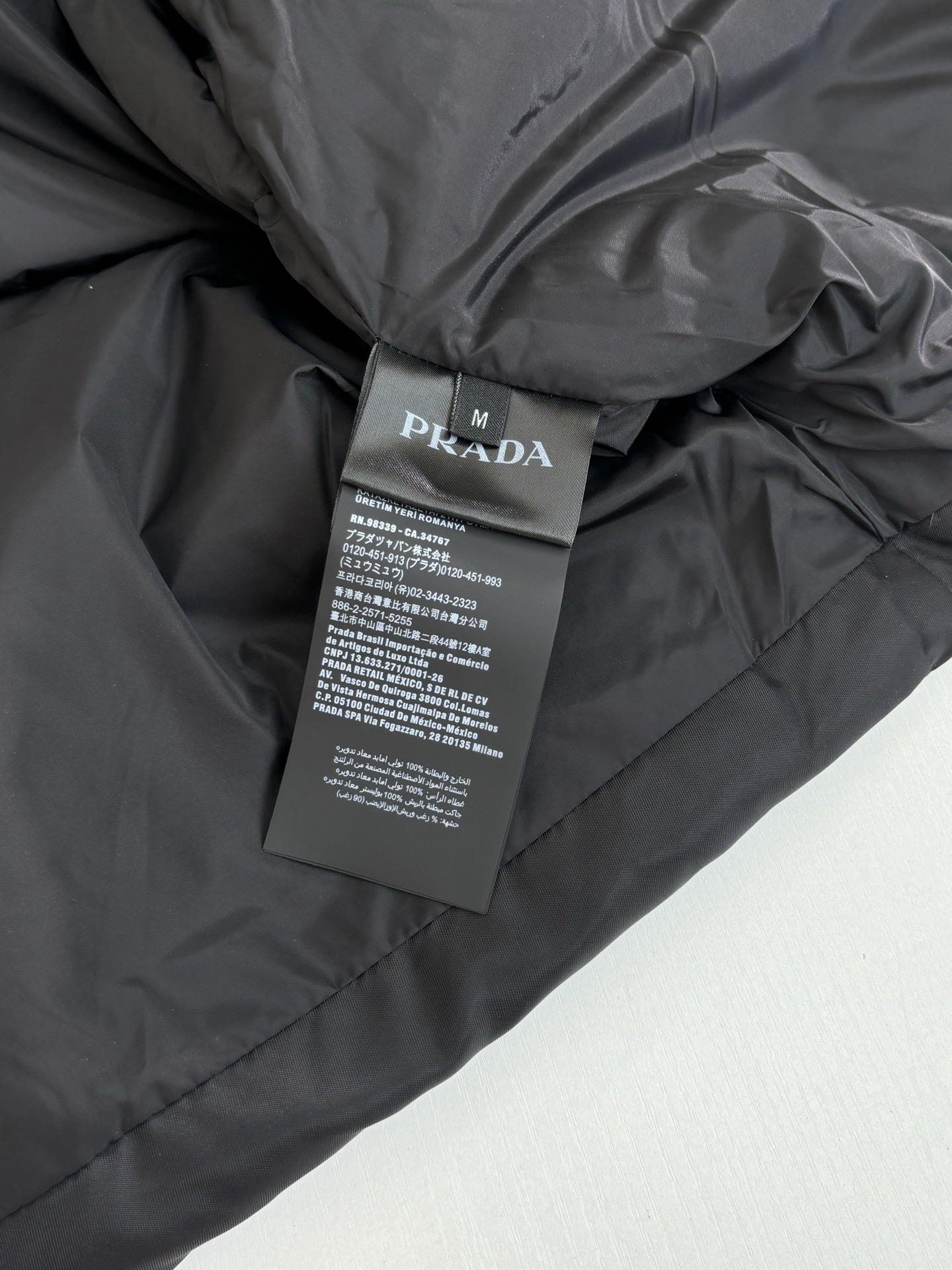 Prad*/普拉达 翻袋倒三角铁牌羽绒外套再生尼龙面料材质，再生尼龙面料也被称为尼龙回料，是一种环保面料