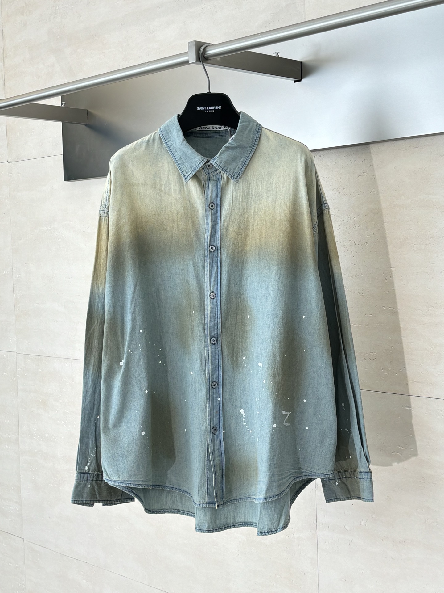 NO:539839,ACNE Studio* 25FW ink-splashing old denim shirt uses high-weight, high-density cotton denim fabric as the base for creation. The fabric itself has been specially treated, with a delicate and solid texture and a unique background color, providing the best adhesion surface and color contrast for subsequent manual craftsmanship, ensuring the clear and long-lasting effect of the ink splashing effect. The ink splashing pattern on each shirt is completed by hand painting. Manual operation controls the layering and changes in the ink color. By adjusting the distance, strength and pigment concentration of the spray painting, it creates a full and strong ink core and a gentle and elegant ink halo, avoiding the stiffness and dullness of machine printing. After partial fading before ink splashing, a natural aging effect is formed at the collar, shoulder lines, cuffs, etc., and jointly creates a sense of narrative that has gone through time and is free and unruly.  The back glue screen printing will form a slightly convex and rubbery coating on the surface of the fabric, which together form a rich triple tactile layer with the soft touch of the fabric itself and the flatness of the ink splashing area. The buttons are not ordinary auxiliary materials, but exclusively customized 'tarot material' grey buttons. The natural material has a dark pattern or a unique luster similar to the mysterious tarot card. The color and texture of each button are uniformly screened to ensure a high degree of harmony with the overall color atmosphere of the shirt, reflecting the brand's ultimate pursuit of details. Size44/46/48,,acne studios,dior,shirts,alexander wang19860909ACNE Studio* 25FW 泼墨做旧牛仔衬衫 采用高克重、高密度的全棉牛仔面料作为创作的基底.其面料本身经过特殊处理,拥有细腻而坚实的肌理和独特的底色,为后续的手工工艺提供了最佳的附着面和色彩对比度,确保泼墨效果的清晰和持久.每一件衬衫上的泼墨图案都经由手工涂绘完成.手工操作控制墨色的层次感和虚实变化,通过调节喷绘的距离、力度和颜料浓度,创造出既有饱满浓烈的墨核,又有轻柔飘逸的墨晕的通透效果,避免了机器印花的生硬与呆板. 在泼墨前经过局部褪色处理,在衣领、肩线、袖口等处形成自然做旧效果,与泼墨图案共同构筑一种历经岁月、自由不羁的叙事感. 后背胶浆丝网印花,胶浆会在织物表面形成一层微凸的、具有橡胶质感的涂层,与面料本身柔软的触感以及泼墨区域的平坦感,共同构成了丰富的三重触觉层次. 纽扣并非普通辅料,而是专属定制的“塔罗材质”焗灰色纽扣.经过特殊处理的天然材质,表面拥有类似神秘塔罗牌般的暗纹或独特光泽. 每颗纽扣的色泽与质感都经过统一筛选,确保与衬衫的整体色彩氛围达成高度和谐,体现了品牌对细节的极致追求. Size44/46/48,,acne studios,dior,shirts,alexander wang,Men's clothing