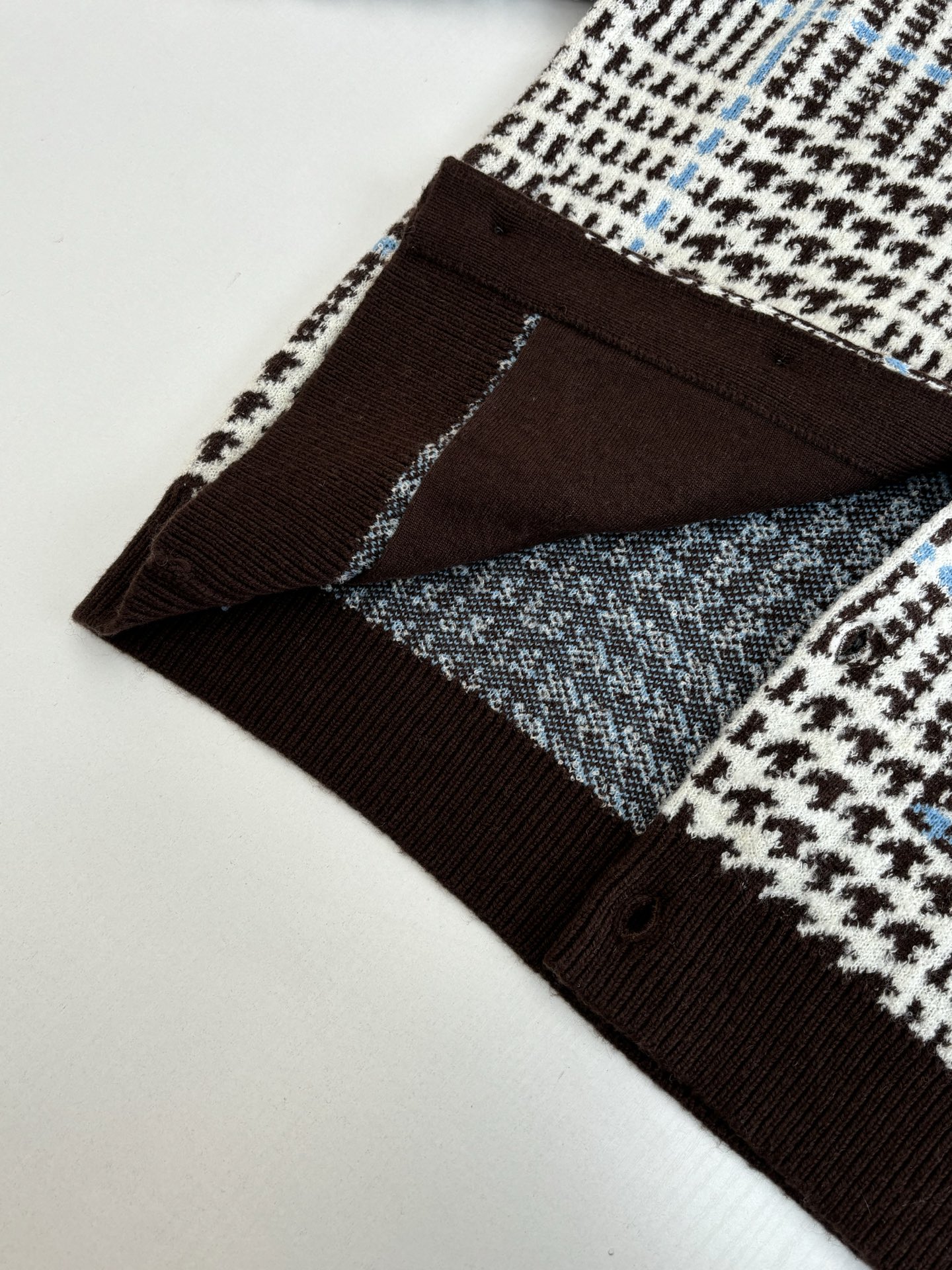 P265
1V/路易 SS26 早春新款 字母嵌花千鸟格针织提花开衫

本款开衫采用全幅提花工艺织造主体图案，以69%绵羊毛混纺31%锦纶的纱线，将千鸟格纹与淡蓝色线条肌理交织呈现，同时通过嵌花工艺在衣身融入品牌标识元素，图案边缘衔接细腻无断层。领口、袖口及下摆选用100%绵羊毛罗纹面料，采用双针锁边工艺收边，兼具弹性与定型效果。前襟配备天然质感纽扣，侧缝口袋采用隐形车线工艺，与衣身提花纹理自然融合。整体版型通过立体剪裁定型，肩部采用无痕缝合工艺，确保穿着贴合度与舒适度，全件由意大利工坊手工细节收尾，呈现高质感针织单品的工艺精度。整体走线平直细腻，面料舒适柔软，颜色一致无色差 能与同款搭配营造时尚造型，驾驭各种场合，定制辅料，三标齐全，男女同款！

Size：S/M/L/XL