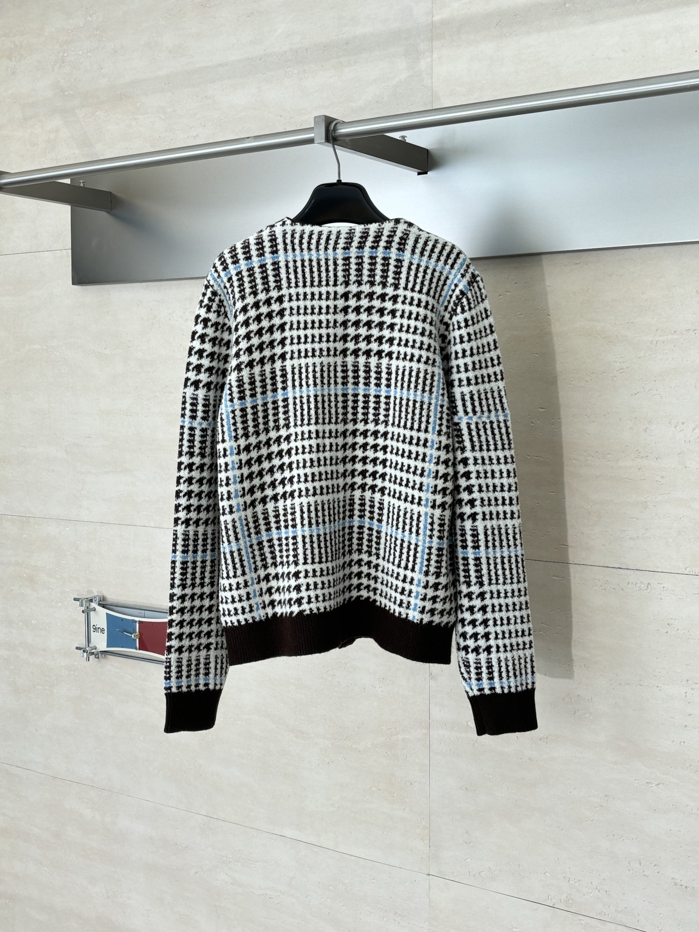 P265
1V/路易 SS26 早春新款 字母嵌花千鸟格针织提花开衫

本款开衫采用全幅提花工艺织造主体图案，以69%绵羊毛混纺31%锦纶的纱线，将千鸟格纹与淡蓝色线条肌理交织呈现，同时通过嵌花工艺在衣身融入品牌标识元素，图案边缘衔接细腻无断层。领口、袖口及下摆选用100%绵羊毛罗纹面料，采用双针锁边工艺收边，兼具弹性与定型效果。前襟配备天然质感纽扣，侧缝口袋采用隐形车线工艺，与衣身提花纹理自然融合。整体版型通过立体剪裁定型，肩部采用无痕缝合工艺，确保穿着贴合度与舒适度，全件由意大利工坊手工细节收尾，呈现高质感针织单品的工艺精度。整体走线平直细腻，面料舒适柔软，颜色一致无色差 能与同款搭配营造时尚造型，驾驭各种场合，定制辅料，三标齐全，男女同款！

Size：S/M/L/XL