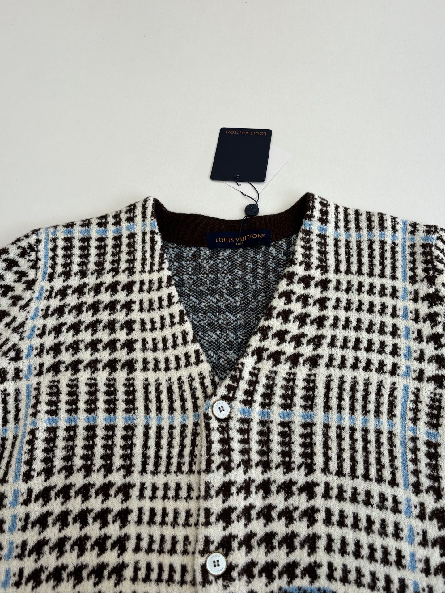 P265
1V/路易 SS26 早春新款 字母嵌花千鸟格针织提花开衫

本款开衫采用全幅提花工艺织造主体图案，以69%绵羊毛混纺31%锦纶的纱线，将千鸟格纹与淡蓝色线条肌理交织呈现，同时通过嵌花工艺在衣身融入品牌标识元素，图案边缘衔接细腻无断层。领口、袖口及下摆选用100%绵羊毛罗纹面料，采用双针锁边工艺收边，兼具弹性与定型效果。前襟配备天然质感纽扣，侧缝口袋采用隐形车线工艺，与衣身提花纹理自然融合。整体版型通过立体剪裁定型，肩部采用无痕缝合工艺，确保穿着贴合度与舒适度，全件由意大利工坊手工细节收尾，呈现高质感针织单品的工艺精度。整体走线平直细腻，面料舒适柔软，颜色一致无色差 能与同款搭配营造时尚造型，驾驭各种场合，定制辅料，三标齐全，男女同款！

Size：S/M/L/XL