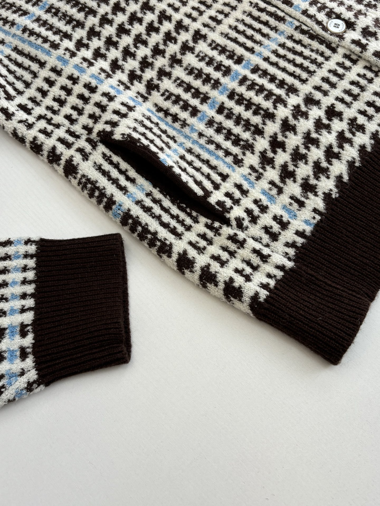 P265
1V/路易 SS26 早春新款 字母嵌花千鸟格针织提花开衫

本款开衫采用全幅提花工艺织造主体图案，以69%绵羊毛混纺31%锦纶的纱线，将千鸟格纹与淡蓝色线条肌理交织呈现，同时通过嵌花工艺在衣身融入品牌标识元素，图案边缘衔接细腻无断层。领口、袖口及下摆选用100%绵羊毛罗纹面料，采用双针锁边工艺收边，兼具弹性与定型效果。前襟配备天然质感纽扣，侧缝口袋采用隐形车线工艺，与衣身提花纹理自然融合。整体版型通过立体剪裁定型，肩部采用无痕缝合工艺，确保穿着贴合度与舒适度，全件由意大利工坊手工细节收尾，呈现高质感针织单品的工艺精度。整体走线平直细腻，面料舒适柔软，颜色一致无色差 能与同款搭配营造时尚造型，驾驭各种场合，定制辅料，三标齐全，男女同款！

Size：S/M/L/XL