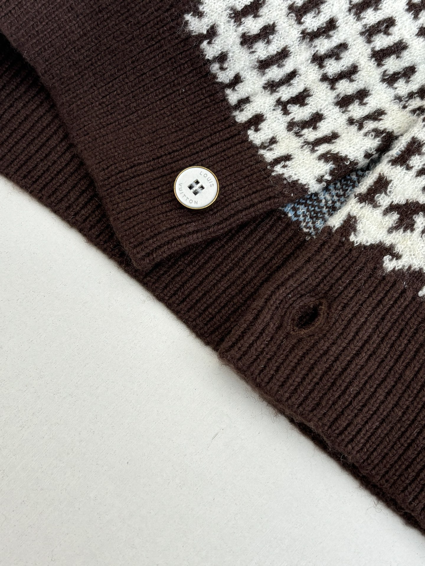 P265
1V/路易 SS26 早春新款 字母嵌花千鸟格针织提花开衫

本款开衫采用全幅提花工艺织造主体图案，以69%绵羊毛混纺31%锦纶的纱线，将千鸟格纹与淡蓝色线条肌理交织呈现，同时通过嵌花工艺在衣身融入品牌标识元素，图案边缘衔接细腻无断层。领口、袖口及下摆选用100%绵羊毛罗纹面料，采用双针锁边工艺收边，兼具弹性与定型效果。前襟配备天然质感纽扣，侧缝口袋采用隐形车线工艺，与衣身提花纹理自然融合。整体版型通过立体剪裁定型，肩部采用无痕缝合工艺，确保穿着贴合度与舒适度，全件由意大利工坊手工细节收尾，呈现高质感针织单品的工艺精度。整体走线平直细腻，面料舒适柔软，颜色一致无色差 能与同款搭配营造时尚造型，驾驭各种场合，定制辅料，三标齐全，男女同款！

Size：S/M/L/XL