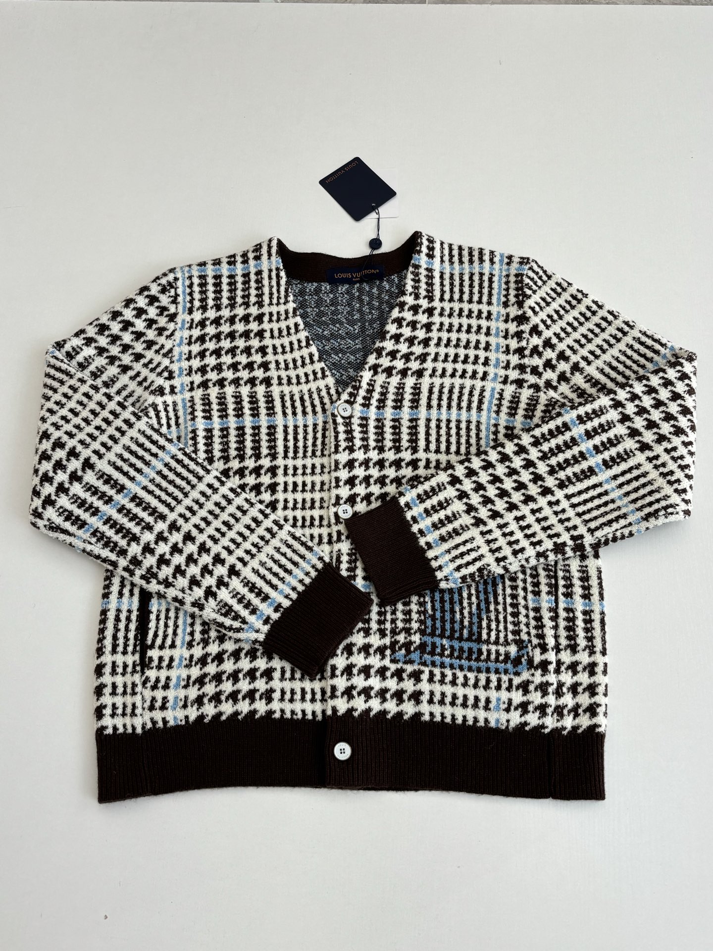 P265
1V/路易 SS26 早春新款 字母嵌花千鸟格针织提花开衫

本款开衫采用全幅提花工艺织造主体图案，以69%绵羊毛混纺31%锦纶的纱线，将千鸟格纹与淡蓝色线条肌理交织呈现，同时通过嵌花工艺在衣身融入品牌标识元素，图案边缘衔接细腻无断层。领口、袖口及下摆选用100%绵羊毛罗纹面料，采用双针锁边工艺收边，兼具弹性与定型效果。前襟配备天然质感纽扣，侧缝口袋采用隐形车线工艺，与衣身提花纹理自然融合。整体版型通过立体剪裁定型，肩部采用无痕缝合工艺，确保穿着贴合度与舒适度，全件由意大利工坊手工细节收尾，呈现高质感针织单品的工艺精度。整体走线平直细腻，面料舒适柔软，颜色一致无色差 能与同款搭配营造时尚造型，驾驭各种场合，定制辅料，三标齐全，男女同款！

Size：S/M/L/XL