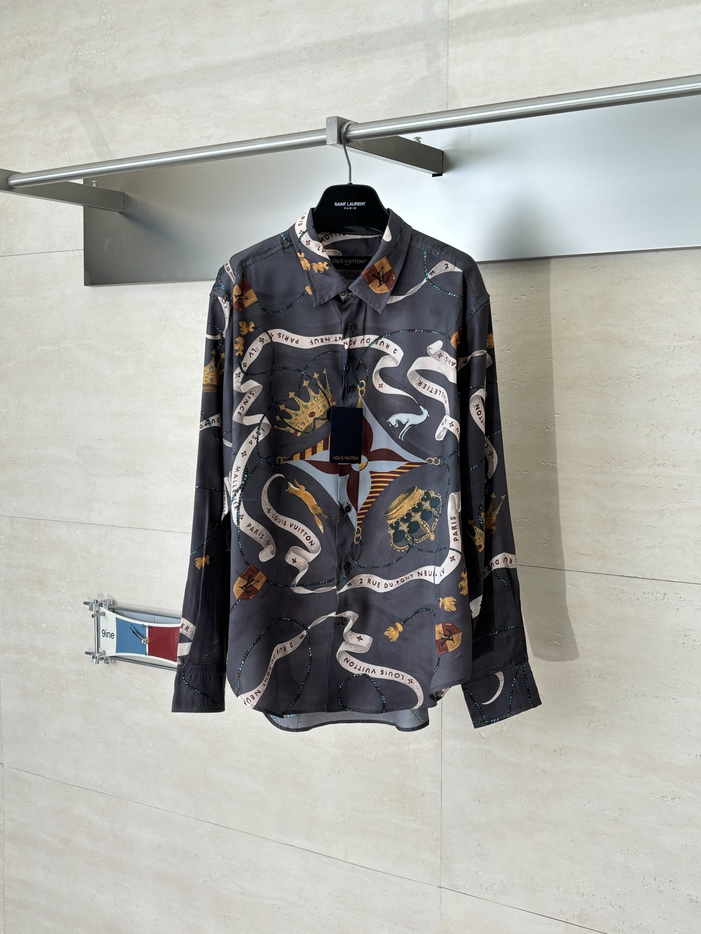 NO:685101,1V/Louis FW25 crown ribbon contrasting mulberry silk lapel long-sleeved shirt  This printed long-sleeved shirt is made of 19mm mulberry silk and cotton blended fabric, made through high-density woven technology. The fabric combines the smooth luster of silk with the crisp and breathable properties of cotton, and has excellent wrinkle resistance and drape. The body printing uses digital direct printing combined with manual color screen printing process. First, digital direct printing is used to restore the delicate texture and gradient color of crowns, ribbons and other patterns, and then manual color screen printing is used to superimpose metallic ink to make the pattern relief three-dimensional.  The texture and gloss are more prominent. After high-temperature fixation and washing tests, the color fastness reached level 4 or above. The collar of the shirt adopts an inlaid collar design, which is matched with high-temperature pressing and shaping technology. The collar is stiff and not easy to deform; the placket is handmade  The overlocking process and the buttons are made of natural horn buttons, each of which is polished by hand; the side seams are made of French double-needle chain stitching, and the cuffs are designed with adjustable cuffs, showing fine craftsmanship in every detail. The overall routing is straight and delicate.  SizeS/M/L/XL,,louis vuitton,shirts,real silk,198609091V/路易 FW25 皇冠飘带撞色桑蚕丝翻领长袖衬衫 这款印花长袖衬衫选用19姆米桑蚕丝与棉混纺面料,经高密梭织工艺打造,面料兼具真丝的柔滑光泽与棉的挺括透气特性,抗皱性与垂坠感俱佳.衣身印花采用数码直喷结合手工套色丝网印工艺,先以数码直喷还原皇冠、丝带等图案的细腻纹理与渐变色彩,再通过手工套色丝网印叠加金属质感油墨,让图案的浮雕立体感与光泽度更突出,经高温固色与水洗测试,色彩牢度达到4级以上.衬衫领部采用嵌线式领座设计,搭配高温压烫定型工艺,领型挺括不易变形；门襟为手工锁边的包边工艺,纽扣选用天然牛角扣,每颗均经手工打磨抛光；侧缝采用法式双针锁链缝,袖口为可调节袖克夫设计,细节处尽显精工质感.整体走线平直细腻 SizeS/M/L/XL,,louis vuitton,shirts,real silk,,Men's clothing