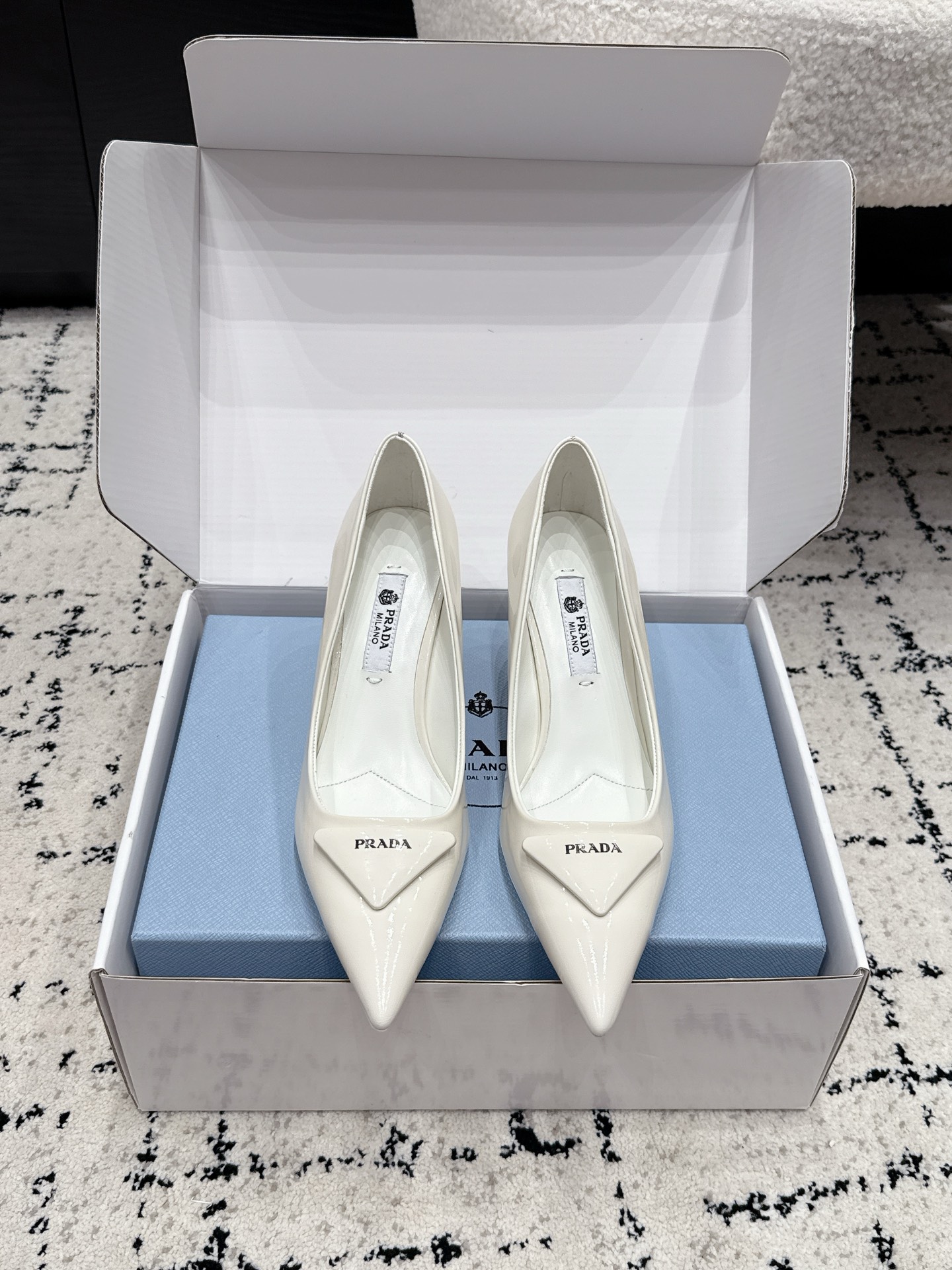 NO:884313,Prada 26/ss classic triangular pointed toe small high-heeled shoes use a combination of sharp pointed toe + geometric triangle logo. The triangular splicing at the toe is a brand-recognizable design, which elongates the leg line and strengthens the sense of pioneering. The heel is a stiletto heel style, which enhances elegance while maintaining the neatness of the shoe shape.  The body of the shoe adopts a simple, non-decorative design, only the brand's iconic triangle element is retained on the toe, and the PRADA logo is engraved on the inside of the shoe. The shoemaking process ensures the comfort and stiffness of the fit for the foot. The upper is made of beaded cowhide/patent leather, the lining is sheepskin, and the outsole is genuine leather. It is increased by 7.5cm. Size #35-41 (customized sizes 40 and 41 are not returnable). High-heeled sandals, prada, prada, sandals, high  heels,cowhide,sheepskin,Leather soles19860909Prada 普拉达 26/ ss 经典款三角标尖头小高跟单鞋 采用锐利尖头+几何三角标的组合,鞋头处的三角拼接是品牌辨识度设计,拉长腿部线条的同时强化了先锋感；鞋跟为细高跟款式,提升优雅气质的同时保持了鞋型的利落感. 鞋身采用简约的无装饰设计,仅在鞋头处保留品牌标志性三角元素,鞋内印刻PRADA标识,制鞋工艺保障了贴合脚型的舒适度与版型挺括度. 鞋面开标珠牛皮/漆皮 内里羊皮 大底真皮大底 增高7.5cm size#35-41码（40、41码定制不退换）,高跟鞋凉鞋,prada,prada,sandals,high heels,cowhide,sheepskin,Leather soles,Women's Shoes