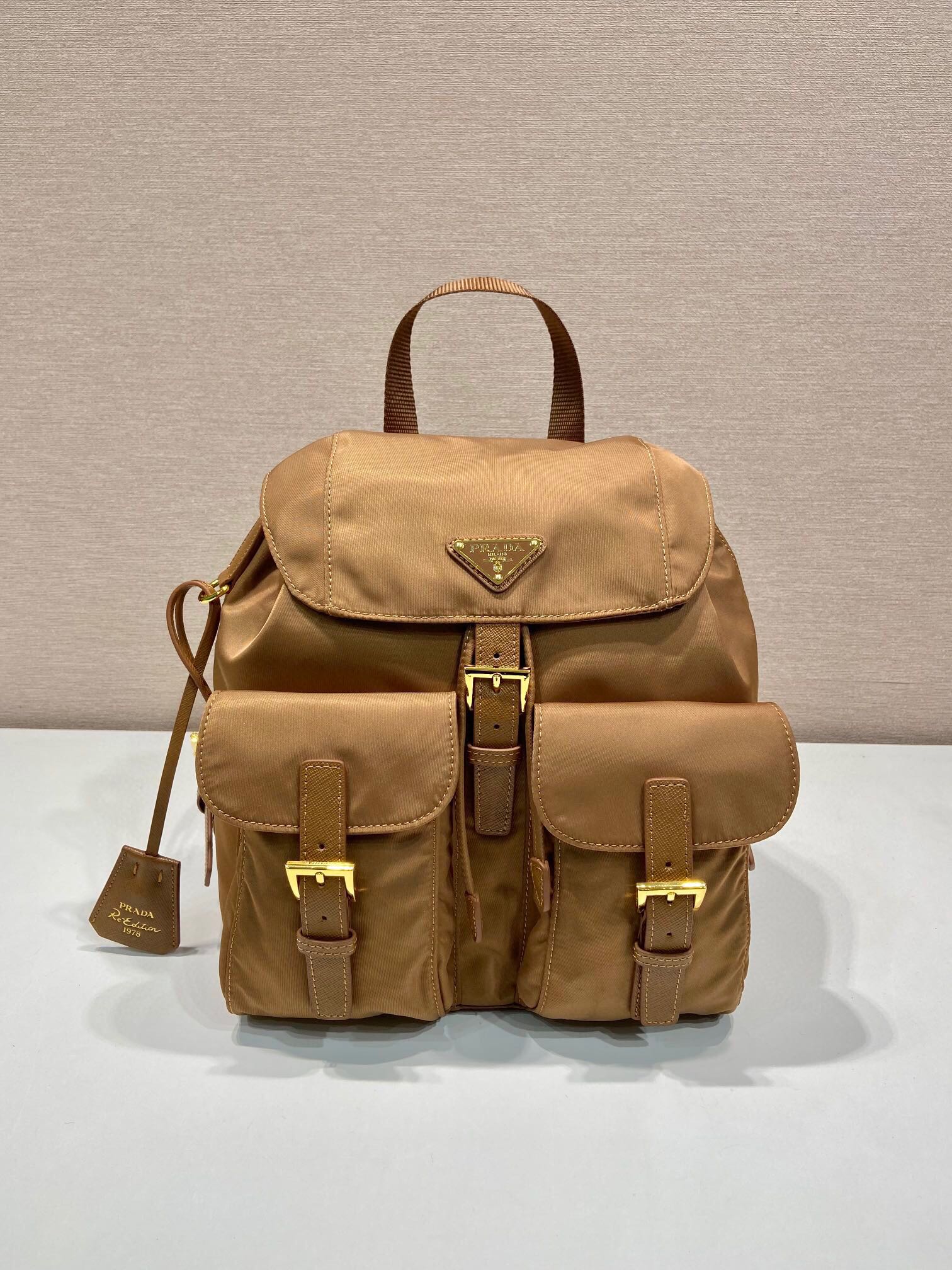 P Family Small Backpack 1BZ677. This women's backpack features imported waterproof fabric, premium hardware, and adjustable fabric straps. Drawstring flap design with one zippered pocket and one magnetic patch pocket inside. Spacious and ultra-lightweight. Dimensions: 28 x 23.5 x 12 cm. 007650 image 1