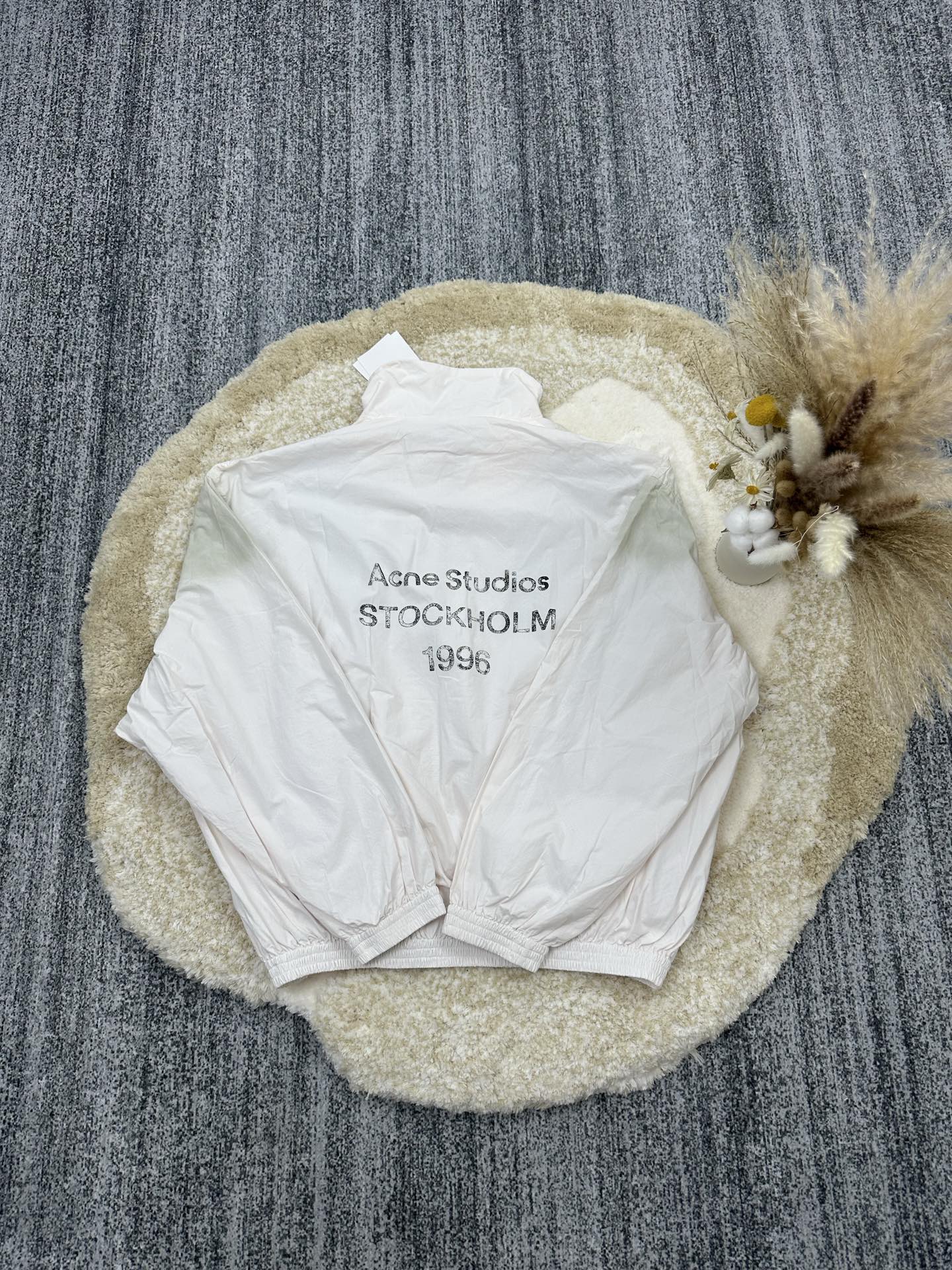 P290,全网顶级版本
Acne Studios 撞色徽标拉链夹克

定制幻光雅棉细织绸 柔软丝滑 舒适贴肤 以泛黄的米白为色调 那不经意间晕染的做旧效果 邂逅复古情怀载体 幅饰以同质化展示 搭配后幅醒目的 Acne Studios 1996撞色徽标点缀 既有着复古的韵味 又散发着现代的简约时尚感 松紧袖口和下摆设计 巧妙地勾勒出身体线条 在随性中透露出无法忽视的高级感 是街头最具格调的时尚先锋

采用固体印花 胸前印花经过三次菲林网板修改 使用胶浆液体涂料在织物上打印图案 烘烤织物以固定印刷图案

渐变做旧喷马骝工艺 通过在织物表面喷洒不同颜色的染料 实现衣物在不同光线下呈现出丰富的色彩变化 增加视觉层次感

重度孝洗 通过特制溶液 去除污渍且轻微的褪色 再雪花洗 通过强烈的洗涤方式来褪色 使其颜色更为均匀

下摆采用三针像筋拉腰机一次而成 利用机器的特殊针位和送料机构 将松紧带与布料在同一工序中缝合在一起 三针的设计更加牢固 能够均匀地分布压力 确保松紧带与布料紧密贴合
尺码： 42 44 46 48