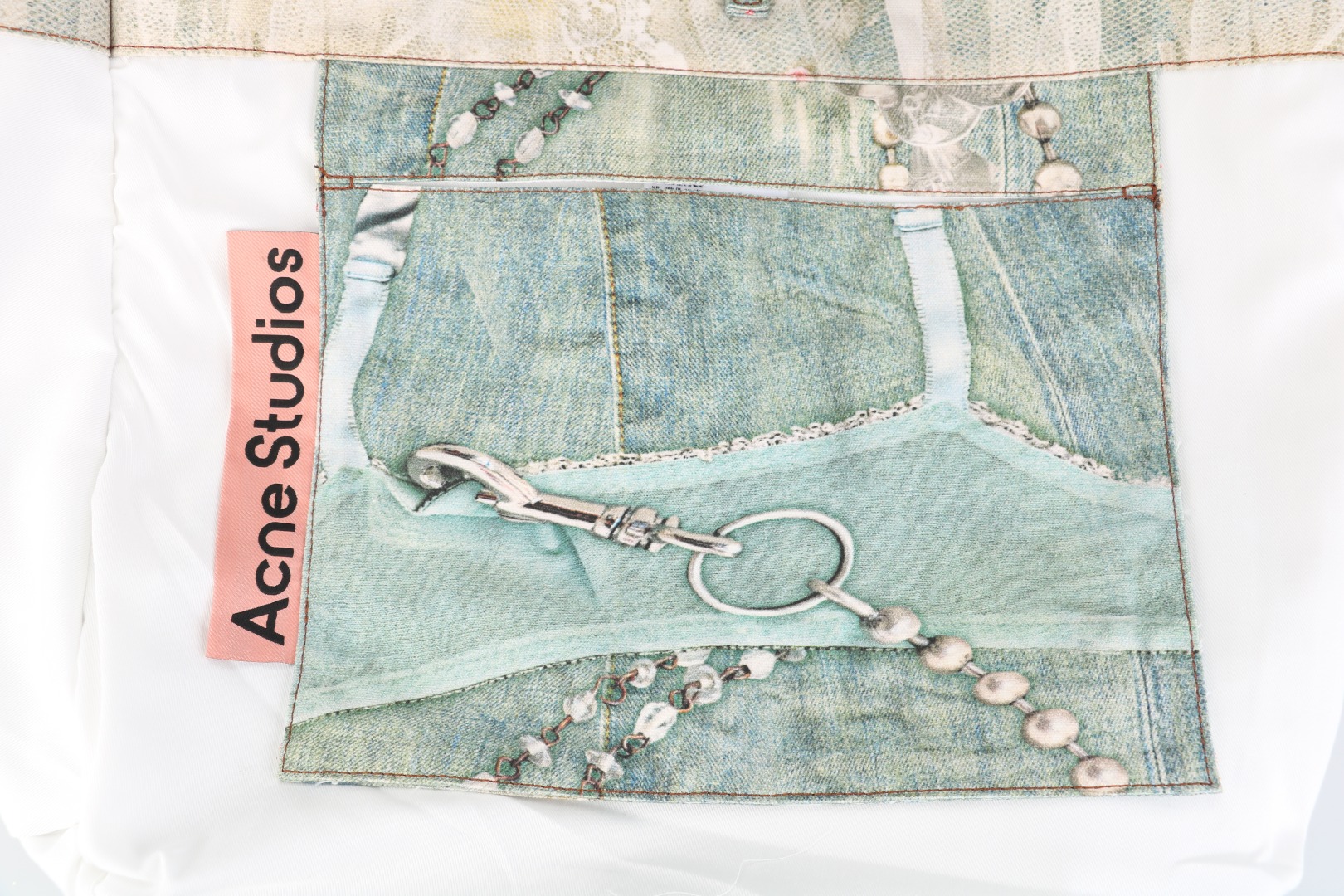 图片[3]-#Acne Studios 25Fw 蕾丝珍珠印花牛仔托特包 采用高密双股纱线织造，克重达420g/㎡，表面呈现粗粝斜纹肌理，同时通过预缩酵素洗处理确保尺寸稳定性，赋予包体挺括骨架感与抗变形性能，选用进口数码直喷机，实现1200dpi高清印花，通过6色纳米墨水层叠渗透技术，将“蕾丝裤”图案以微米级精度附着于帆布纱线间隙，形成立体浮雕触感。匹布印后经UV固化与硅油柔化处理，确保图案耐水洗、抗摩擦，使用兄弟BAS双针平缝机，配置16号钛涂层牛仔针与Tex 70高弹涤纶线，在包体侧缝及底部间距同步车缝双线，形成平行受力通道，分散承重压力。三次元回针加固，在拎手锚点、包角应力区采用电脑程式化回针，配合背面热熔胶衬垫，形成机械-化学双重复合固定，此设计通过材料科学与精密缝制技术的交叉应用，实现柔美意象与重型帆布机能结构的对立统一，体现ACNE对当代工艺美术化的极致追求 尺码：47×17×35-选品中心