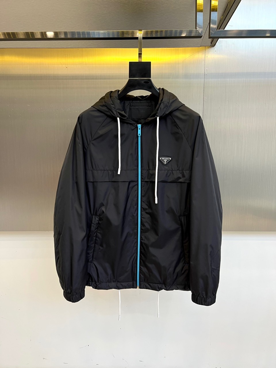 NO:514437,Prad, 25FW black functional style hooded jacket, matte nylon fabric creates lightweight and waterproof performance, the iconic blue zipper and white drawstring collided to create visual tension. The left chest PRADA triangle mark shows its lineage in a low-key way, and the lining label confirms Italian seductive cutting. The metallic glossy background sets off, interpreting the pinnacle of the dark functional aesthetics. 48-56 (model 173, 143 catties upper body 50 yards),,prada,prada,jackets & coats,jackets & coats,hats,alexander wang19860909Prad普拉、25FW黑色机能风连帽夹克外套 哑光尼龙面料打造轻盈防水性能,标志性蓝色拉链与白色抽绳碰撞出视觉张力.左胸PRADA三角标低调彰显血统,内衬标签印证意式精工剪裁.金属光泽背景衬托,诠释暗黑系机能美学的巅峰之作.48-56（模特173,143斤上身50码）,,prada,prada,jackets & coats,jackets & coats,hats,alexander wang,Men's clothing