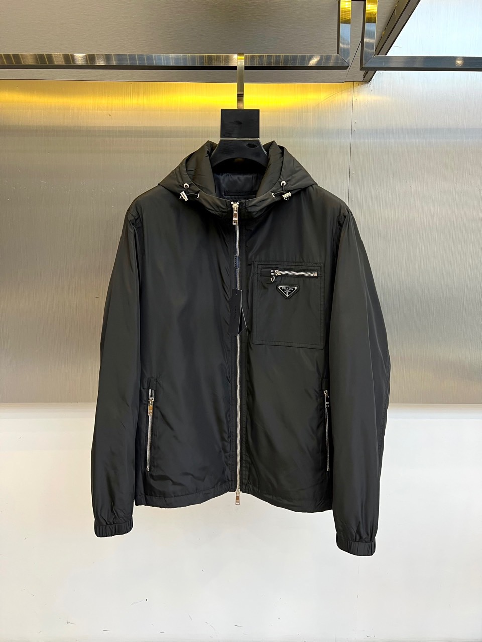 NO:514433,Prad, 25s autumn and winter new olive green hooded jacket | Luxury expression of functional aesthetics Low-key edge, about to break out Cool-tuned olive green nylon fabric flows metallic luster, paired with silver Prada triangle logo, like the edge in the dark night. Three-dimensional chest pockets and metal zippers form geometric lines, elastic rib cuffs are neatly closed, and every detail is a precise balance of function and aesthetics. Urban armor, light appearance, From Modern Building to Midnight Street, this jacket takes 'invisible luxury' as its creed. Windproof nylon material is matched with hooded design, resisting temperature differences, and replaces the exaggerated logo with the glimmer of the material itself - the real style never overshadows the main thing. 48-56 (model 173, 143 catties upper body 50 yards),, prada, prada, jackets & coats, hats, alexander  wang19860909Prad普拉、25s秋冬新品橄榄绿连帽夹克 | 机能美学的奢华表达 低调锋芒,一触即发 冷调橄榄绿尼龙面料流动金属光泽,搭配银色Prada三角徽标,如暗夜中的锋芒.立体胸袋与金属拉链构成几何线条,弹性罗纹袖口利落收束,每一处细节都是功能与美学的精密平衡. 都市装甲,轻盈登场 从摩登大厦到午夜街头,这件夹克以“隐形奢华”为信条.防风尼龙材质搭配连帽设计,抵御温差的同时,用材质本身的微光取代浮夸标识——真正的风格从不喧宾夺主.48-56（模特173,143斤上身50码）,,prada,prada,jackets & coats,hats,alexander wang,Men's clothing