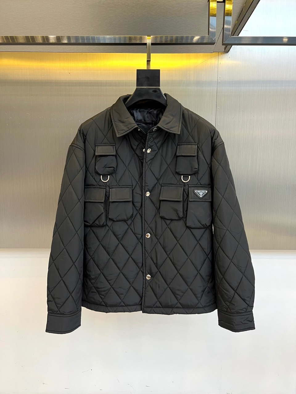 NO:514455,Prad, 25s autumn and winter new black diamond quilted thin cotton jacket jacket. Geometric order, hidden sharpness. Precisely arranged diamond quilting is like a circuit matrix, five matte metal buttons are arranged along the central axis, giving the crisp silhouette a mechanical aesthetic. The functional pocket on the chest is decorated with industrial-style metal rings, and every detail is a rigorous equation of functional aesthetics. When the lapel is erected, it becomes an urban protective shield armor. After the buttons are all set, the neat silhouette reconstructs the body outline. Under the warm yellow light rail of the metal background, each quilting calculates the optimal light refractive angle. High-density nylon locks the temperature with an architecturally-like quilting structure, and its clarity is comparable to the marble columns of the Milan Church. Hanging in front of the metal grid background, the jacket itself is a moving modern art installation.  48-56 (model 173, 143 catties upper body 50 sizes), prada, prada, jackets & coats, jackets & coats, alexander wang19860909Prad普拉、25s秋冬新品黑色菱格纹绗缝薄棉夹克外套. 几何秩序,锋芒暗藏 精密排列的菱格绗缝如电路矩阵,五颗哑光金属纽扣沿中轴线列阵,赋予挺括廓形以机械美感.胸前功能口袋缀以工业风金属环扣,每个细节都是功能美学的严谨方程式. 翻领立起时,化身都市防护盾甲 纽扣全系后,利落剪影重构身体轮廓 金属背景的暖黄光轨下,每道绗缝都在计算最佳光线折射角度 高密度尼龙以建筑般的绗缝结构锁住温度,挺括度堪比米兰教堂的大理石立柱.悬挂于金属网格背景前,这件夹克本身就是移动的现代艺术装置. 48-56（模特173,143斤上身50码）,,prada,prada,jackets & coats,jackets & coats,alexander wang,Men's clothing