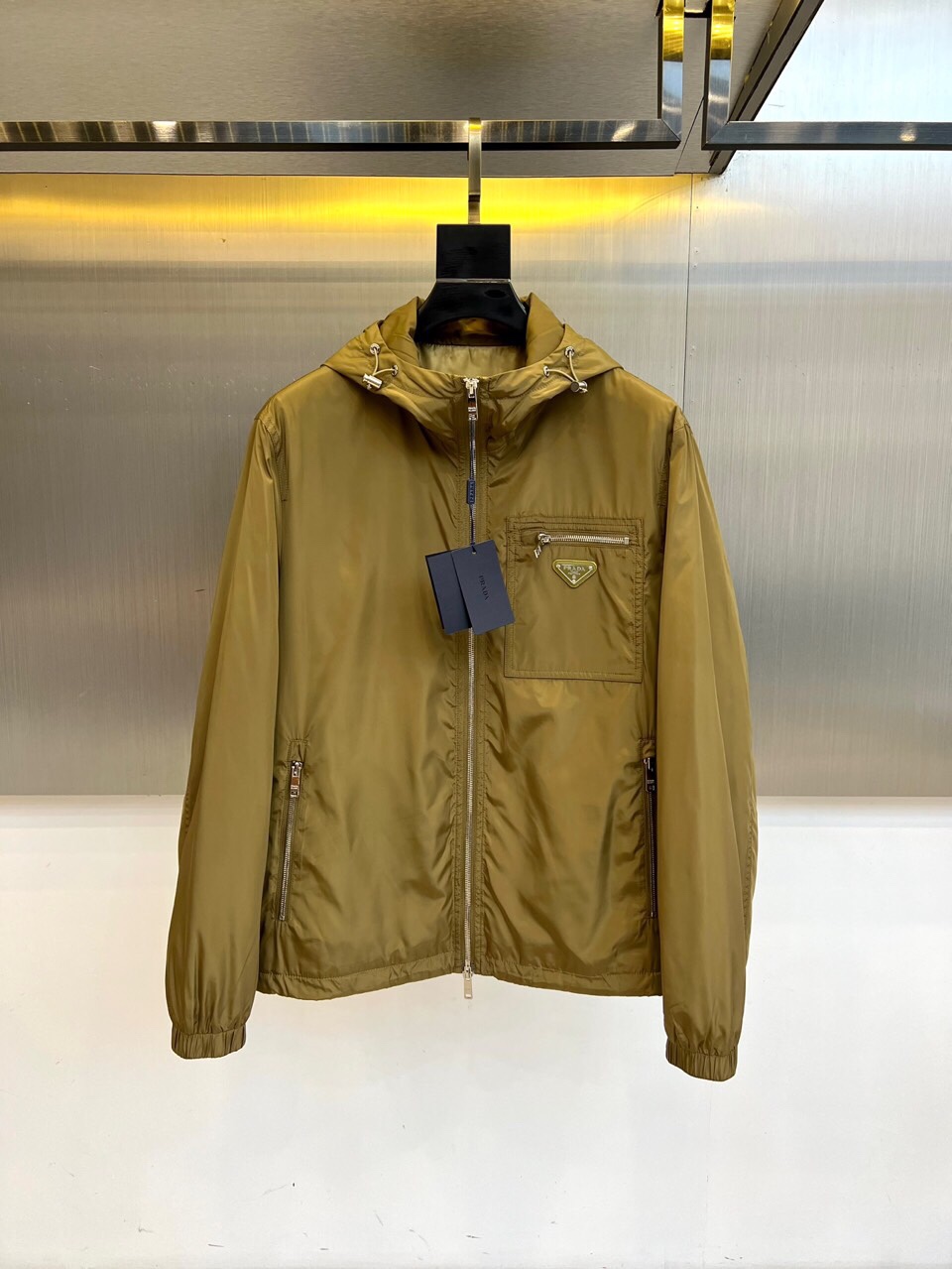 NO:513604,Prad, 25s autumn and winter new olive green hooded jacket | Luxury expression of functional aesthetics Low-key edge, about to break out Cool-tuned olive green nylon fabric flows metallic luster, paired with silver Prada triangle logo, like the edge in the dark night. Three-dimensional chest pockets and metal zippers form geometric lines, elastic rib cuffs are neatly closed, and every detail is a precise balance of function and aesthetics. Urban armor, light appearance, From Modern Building to Midnight Street, this jacket takes 'invisible luxury' as its creed. Windproof nylon material is matched with hooded design, resisting temperature differences, and replaces the exaggerated logo with the glimmer of the material itself - the real style never scatters the main thing. 48-56 (model 173, 143 catties upper body 50 yards),, prada, prada, jackets & coats, hats, alexander  wang19860909Prad普拉、25s秋冬新品橄榄绿连帽夹克 | 机能美学的奢华表达 低调锋芒,一触即发 冷调橄榄绿尼龙面料流动金属光泽,搭配银色Prada三角徽标,如暗夜中的锋芒.立体胸袋与金属拉链构成几何线条,弹性罗纹袖口利落收束,每一处细节都是功能与美学的精密平衡. 都市装甲,轻盈登场 从摩登大厦到午夜街头,这件夹克以“隐形奢华”为信条.防风尼龙材质搭配连帽设计,抵御温差的同时,用材质本身的微光取代浮夸标识——真正的风格从不喧宾夺主.48-56（模特173,143斤上身50码）,,prada,prada,jackets & coats,hats,alexander wang,Men's clothing