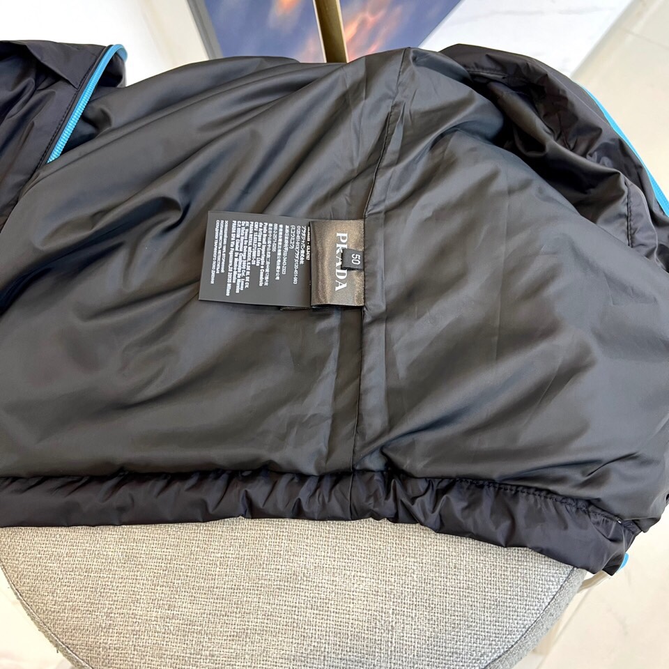 
Prad普拉、25FW黑色机能风连帽夹克外套

哑光尼龙面料打造轻盈防水性能，标志性蓝色拉链与白色抽绳