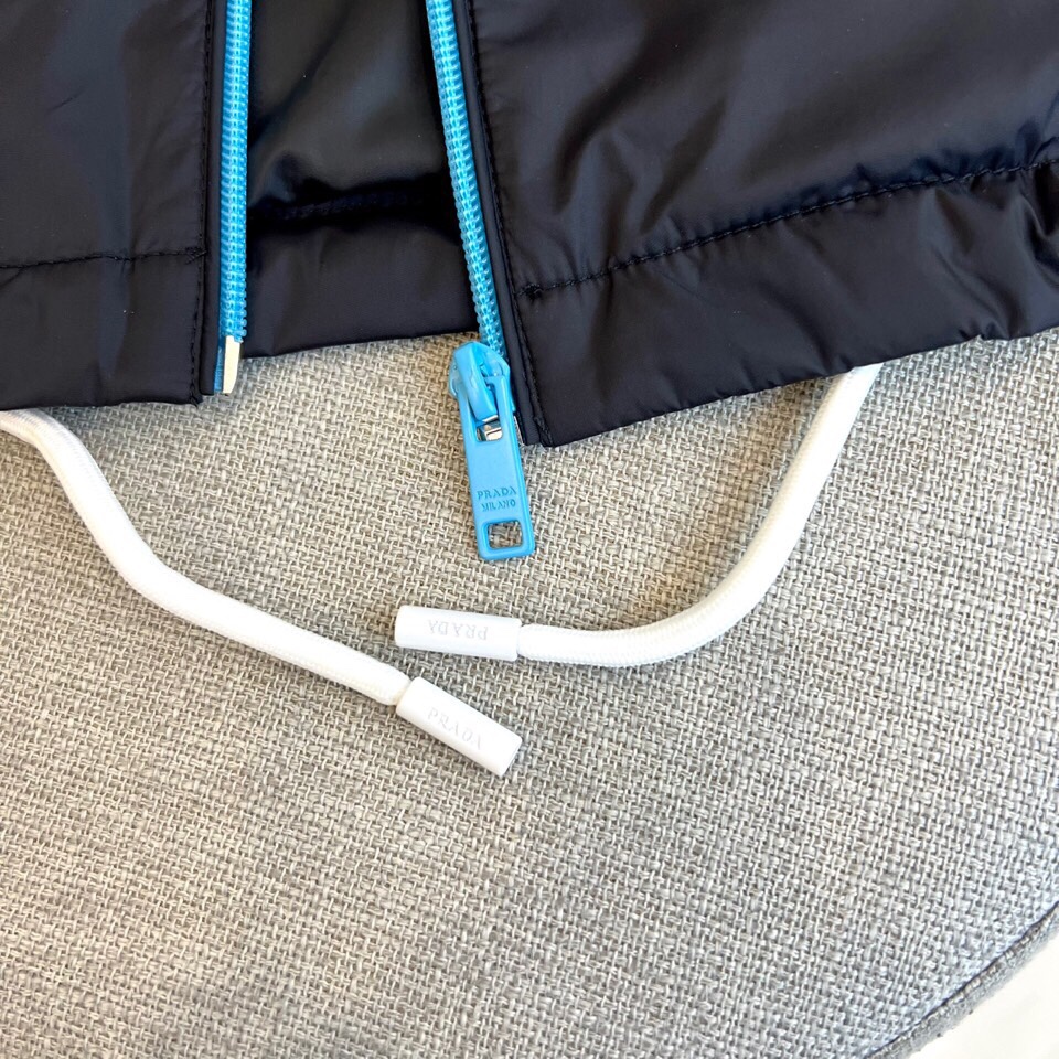 
Prad普拉、25FW黑色机能风连帽夹克外套

哑光尼龙面料打造轻盈防水性能，标志性蓝色拉链与白色抽绳