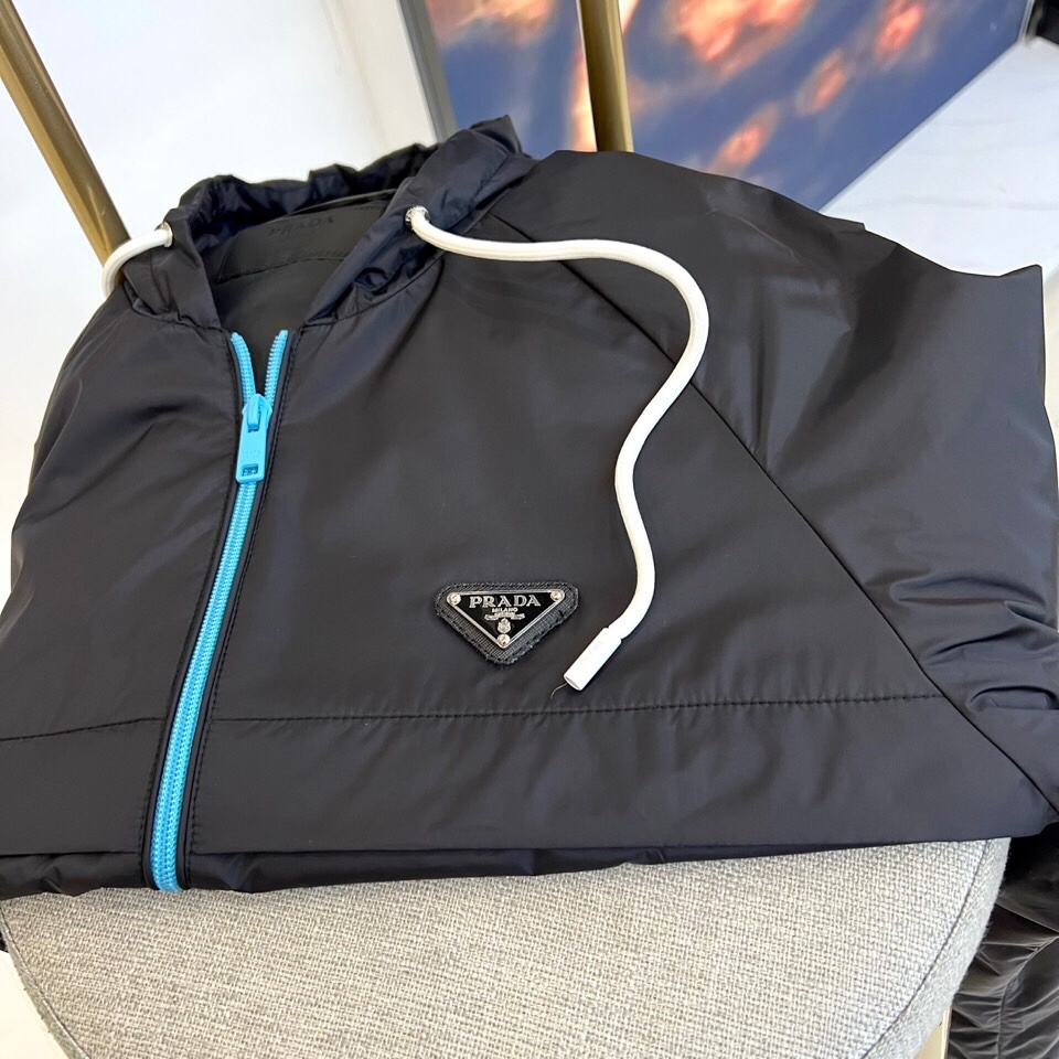 
Prad普拉、25FW黑色机能风连帽夹克外套

哑光尼龙面料打造轻盈防水性能，标志性蓝色拉链与白色抽绳