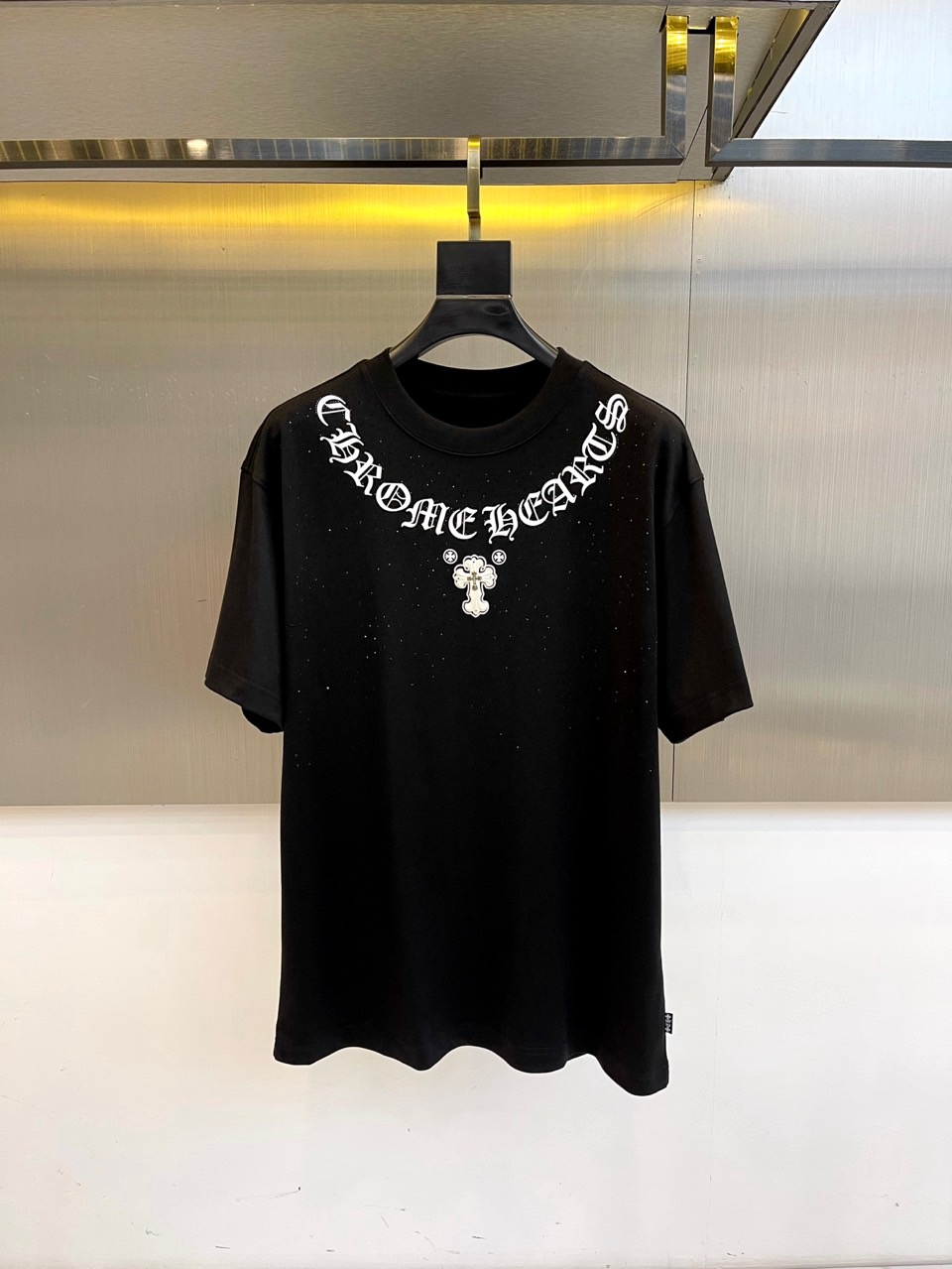 NO:515693,CHROME HEARTS, 2025 autumn and winter mid-sleeved base shirt. The iconic Gothic font 'CHROME HEARTS' and cross totem are branded on the chest. The black hanger is hung on the metal display stand, under the warm yellow spotlight. The screen printing texture of each letter tells the rebellious genes of underground culture. 50 combed cotton viscose fiber blended, passed the GB18401-2010 Class B safety certification. The green 'herbal antibacterial' label in the transparent sealed bag announces the hidden properties of this base shirt - natural plant extract ingredients to achieve dual-effect protection against disease/antibacteriality.  From underground clubs to high-end buyers, this mid-sleeved shirt is both a symbol of faith and a protective armor. It is paired with a leather jacket to reveal the cross totem, or wear it alone to show a complete Gothic slogan. The black declaration on the white canvas will never fade. 48-56 (model 173, 143 catties upper body 50 yards), chrome hearts, chrome hearts, leather jacket, alexander wang19860909CHROME HEARTS克罗心、2025秋冬中袖打底衫.将标志性哥特字体'CHROME HEARTS'与十字架图腾烙于胸前.黑色衣架悬挂于金属展架,暖黄射灯下,每一个字母的丝网印刷纹理都诉说着地下文化的叛逆基因. 50精梳棉粘纤混纺,通过GB18401-2010 B类安全认证.透明密封袋中的绿色「本草抗菌」标签,宣告这件打底衫的隐藏属性——天然植物萃取成分实现抗病/抗菌双效防护. 从地下俱乐部到高端买手店,这件中袖衫既是信仰标记也是防护铠甲.搭配皮衣露出十字架图腾,或单穿展现完整哥特标语,白色画布上的黑色宣言永不褪色.48-56（模特173,143斤上身50码）,,chrome hearts,chrome hearts,leather jacket,alexander wang,Men's clothing