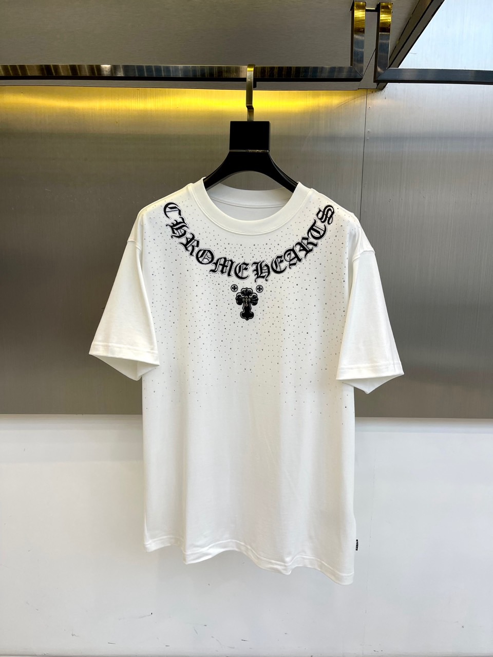 NO:515695,CHROME HEARTS, 2025 autumn and winter mid-sleeved base shirt. The iconic Gothic font 'CHROME HEARTS' and cross totem are branded on the chest. The black hanger is hung on the metal display stand, under the warm yellow spotlight. The screen printing texture of each letter tells the rebellious genes of underground culture. 50 combed cotton viscose fiber blended, passed the GB18401-2010 Class B safety certification. The green 'herbal antibacterial' label in the transparent sealed bag announces the hidden properties of this base shirt - natural plant extract ingredients to achieve dual-effect protection against disease/antibacteriality.  From underground clubs to high-end buyers, this mid-sleeved shirt is both a symbol of faith and a protective armor. It is paired with a leather jacket to reveal the cross totem, or wear it alone to show a complete Gothic slogan. The black declaration on the white canvas will never fade. 48-56 (model 173, 143 catties upper body 50 yards), chrome hearts, chrome hearts, leather jacket, alexander wang19860909CHROME HEARTS克罗心、2025秋冬中袖打底衫.将标志性哥特字体'CHROME HEARTS'与十字架图腾烙于胸前.黑色衣架悬挂于金属展架,暖黄射灯下,每一个字母的丝网印刷纹理都诉说着地下文化的叛逆基因. 50精梳棉粘纤混纺,通过GB18401-2010 B类安全认证.透明密封袋中的绿色「本草抗菌」标签,宣告这件打底衫的隐藏属性——天然植物萃取成分实现抗病/抗菌双效防护. 从地下俱乐部到高端买手店,这件中袖衫既是信仰标记也是防护铠甲.搭配皮衣露出十字架图腾,或单穿展现完整哥特标语,白色画布上的黑色宣言永不褪色.48-56（模特173,143斤上身50码）,,chrome hearts,chrome hearts,leather jacket,alexander wang,Men's clothing