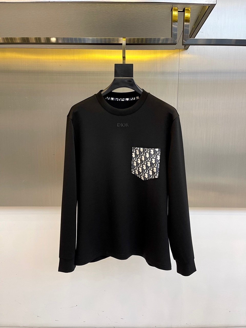 DIO迪奥、2025秋冬长袖T恤卫衣。胸前左侧装饰性口袋与领口内侧的经典老花图案相呼应，正中央