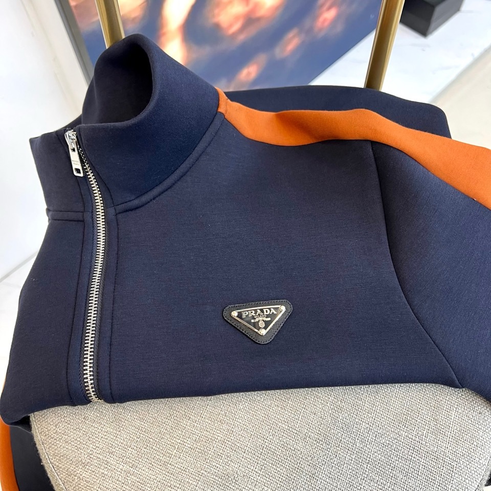 Prad普拉、2025秋冬运动系列。高密弹力面料构筑立体剪裁套装，橙棕条纹如赛道轨迹贯穿袖管与裤线。金属