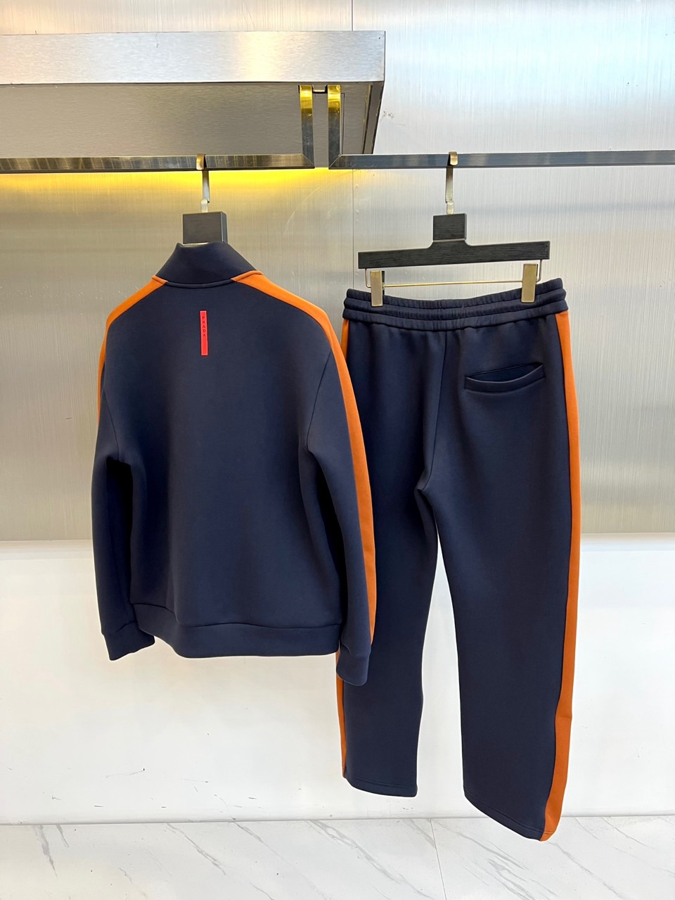 Prad普拉、2025秋冬运动系列。高密弹力面料构筑立体剪裁套装，橙棕条纹如赛道轨迹贯穿袖管与裤线。金属