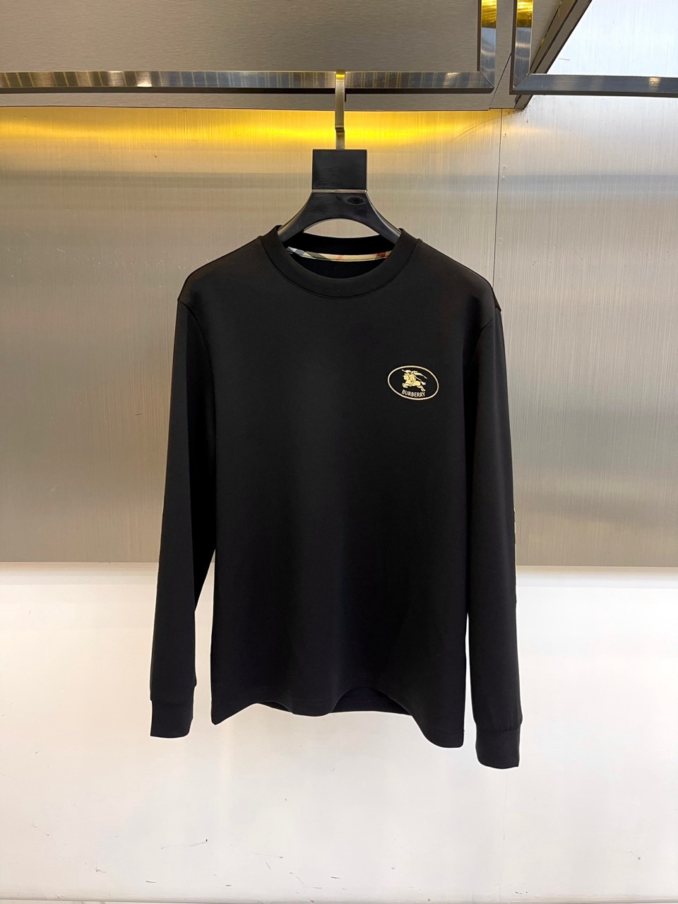 巴宝莉、2025秋冬长袖打底衫。左胸椭圆形金色徽标镌刻品牌基因，领口内侧格纹暗藏经典传承——这是PRAD