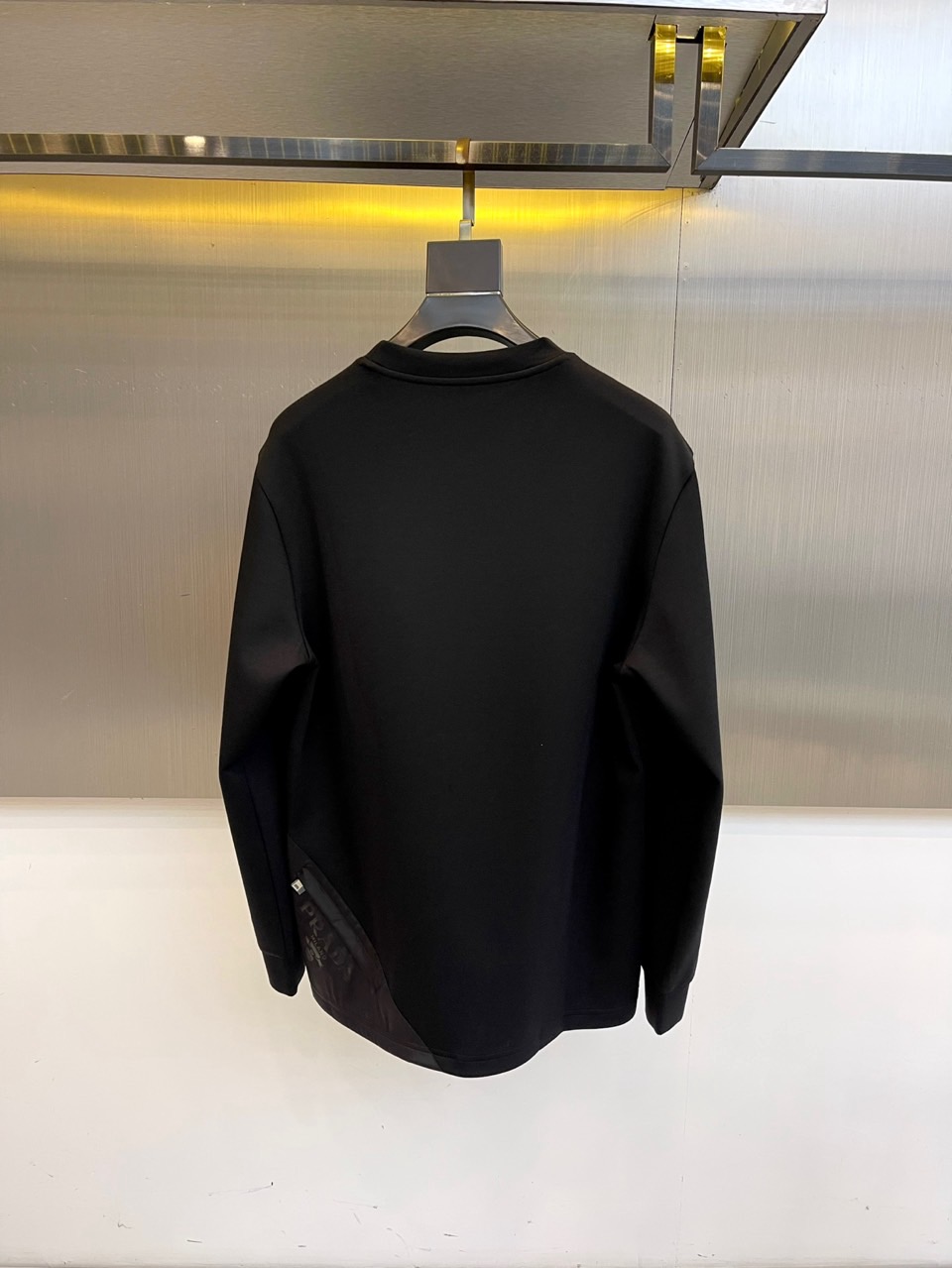 Prad普拉、2025秋冬长袖T恤卫衣。左胸椭圆形金色徽标镌刻品牌基因，领口内侧格纹暗藏经典传承——这是