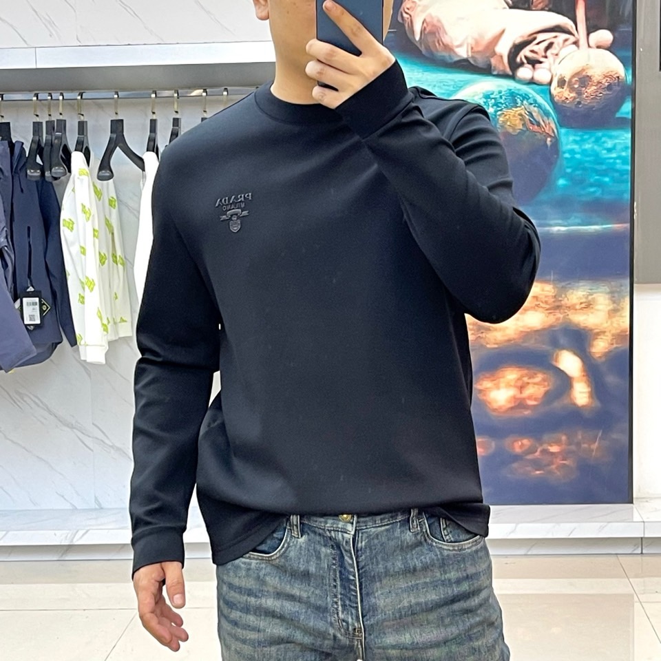 Prad普拉、2025秋冬长袖T恤卫衣。左胸椭圆形金色徽标镌刻品牌基因，领口内侧格纹暗藏经典传承——这是