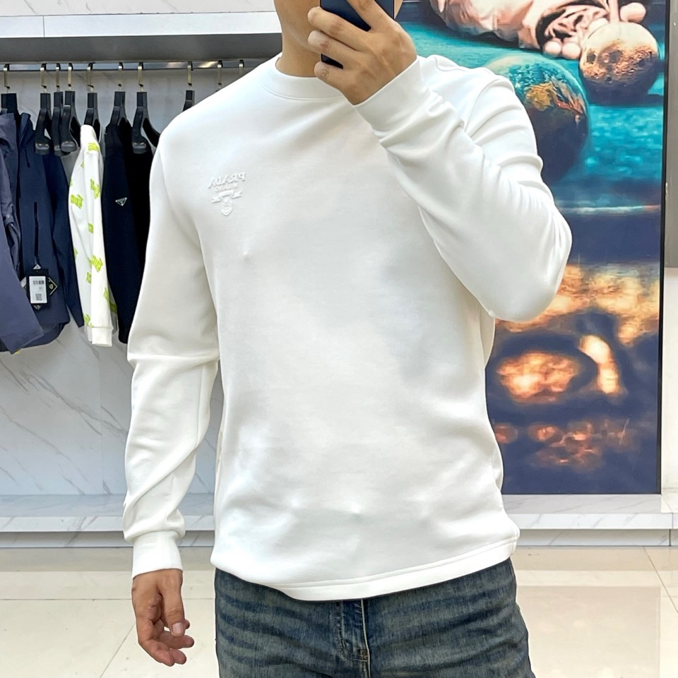 Prad普拉、2025秋冬长袖T恤卫衣。左胸椭圆形金色徽标镌刻品牌基因，领口内侧格纹暗藏经典传承——这是