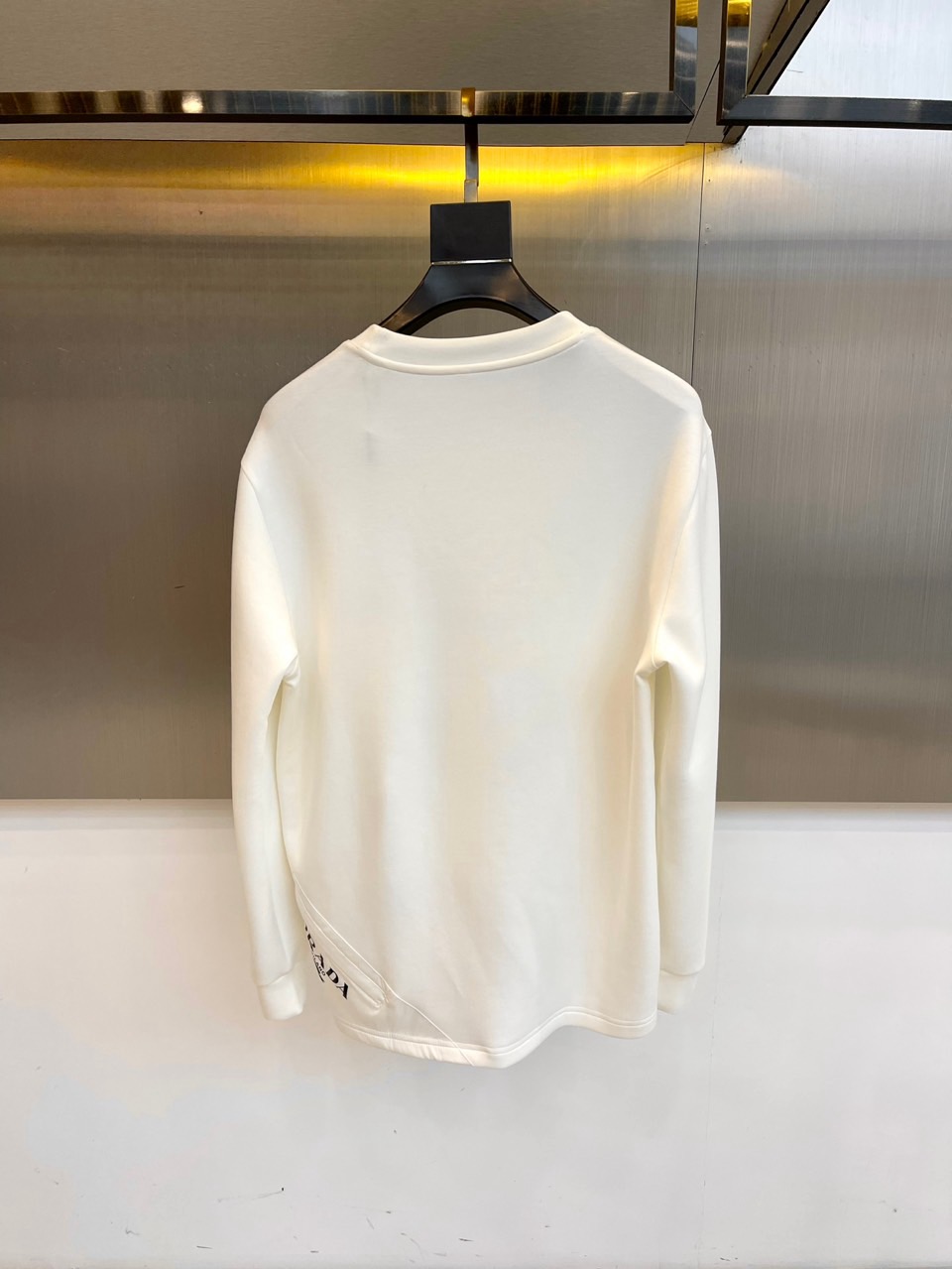 Prad普拉、2025秋冬长袖T恤卫衣。左胸椭圆形金色徽标镌刻品牌基因，领口内侧格纹暗藏经典传承——这是