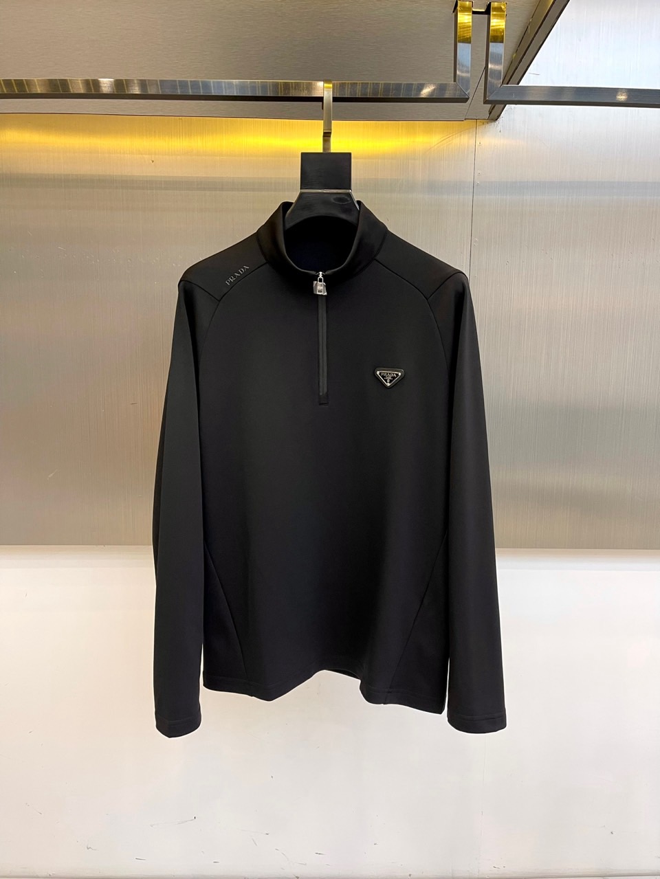 Prad普拉、2025秋冬长袖卫衣T恤。PRADA白色长袖打底衫，以半拉链立领设计诠释现代主义精髓。左胸