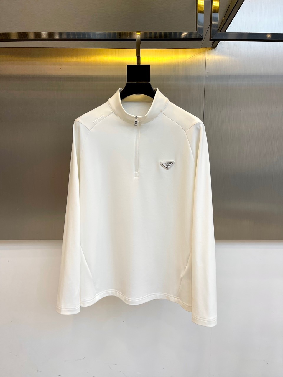 Prad普拉、2025秋冬长袖卫衣T恤。PRADA白色长袖打底衫，以半拉链立领设计诠释现代主义精髓。左胸
