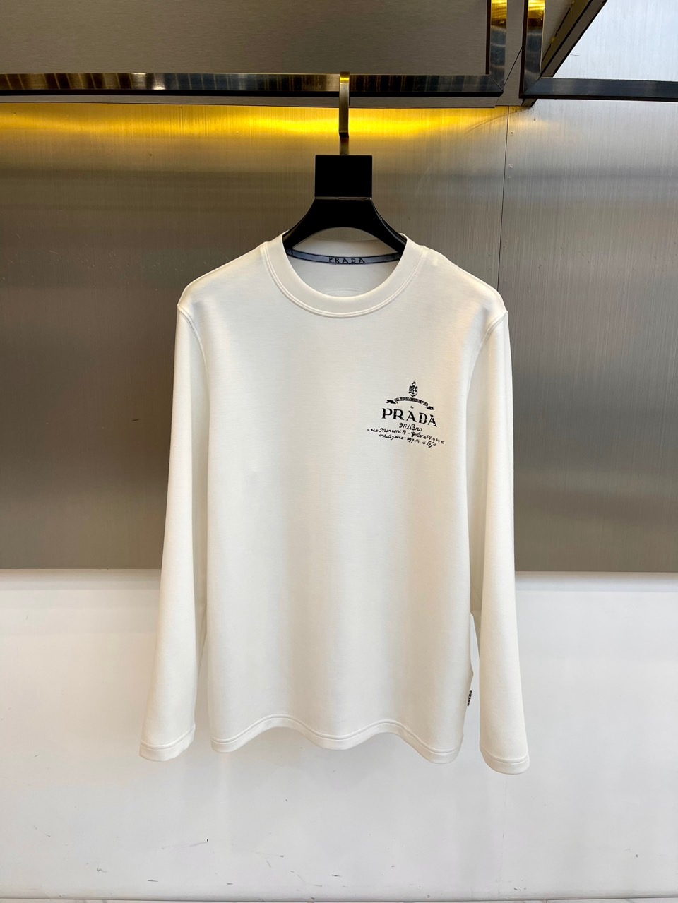 Prad普拉、2025秋冬长袖T恤卫衣。左胸烫金皇冠与手写体