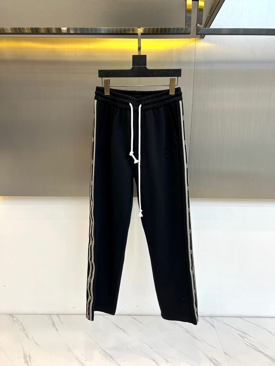 NO:599702,.ALO's new autumn and winter sports trousers, with classic black and white color matching to create a simple and fashionable style. The trousers are made of comfortable fabrics, with an adjustable white drawstring at the waist, taking into account practicality and casual sex. The sides of the trouser legs are decorated with black and white striped designs and are embellished with letter pattern details, adding sporty vitality and layering to the overall look.  The loose and slim fit provides a non-binding wearing experience and is suitable for various occasions such as sports, travel and daily leisure. Whether paired with a sweatshirt to create a sporty style, or combined with a casual top when going out, it can easily present a fashionable and comfortable urban look. M-4XL (model 173,143 pounds, upper body size 50),, hoodie, sweatshirts, alexander wang19860909.ALO 秋冬新品运动长裤,以经典黑白配色打造简约时尚风格.裤子采用舒适面料制成,腰部设计可调节白色抽绳,兼顾实用性与随性感.裤腿两侧饰有黑白相间的条纹设计,并点缀字母图案细节,为整体造型增添运动活力与层次感. 版型宽松垂顺,提供无束缚的穿着体验,适合运动、出行及日常休闲等多种场合.无论是搭配卫衣打造运动风,或与休闲上衣组合出街,都能轻松呈现时髦且舒适的都市造型.M-4XL（模特173,143斤上身50码）,,hoodie,sweatshirts,alexander wang,Men's clothing