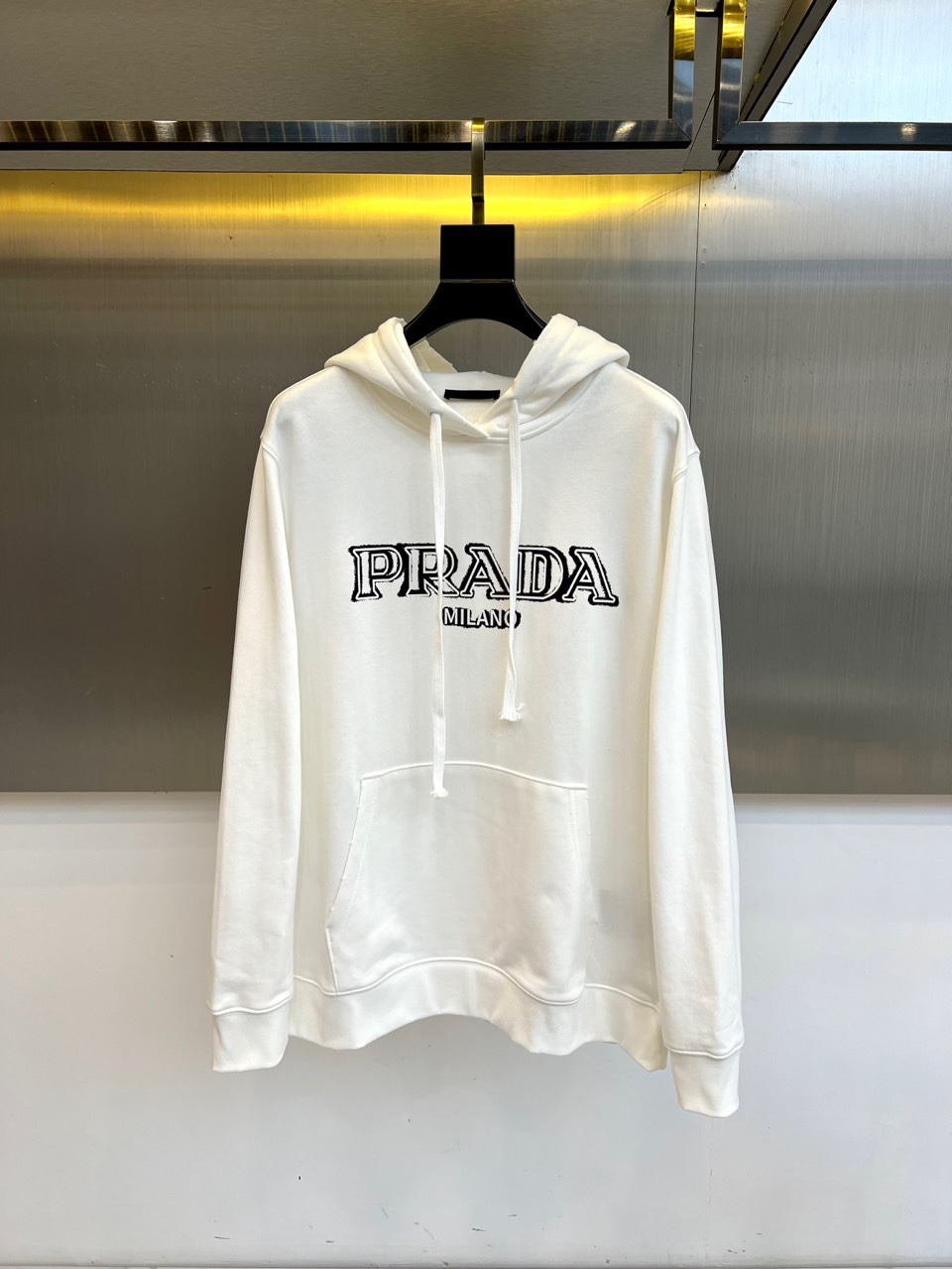 NO:529881,Prada, the new hooded pullover sweatshirt in 2025 autumn and winter, interprets Italian modern aesthetics in a simple white tone. This sweatshirt adopts a classic hooded design and is paired with adjustable drawstrings to balance practicality and fashion. The front is decorated with a striking black 'PRADA MILANO' three-dimensional letter logo, highlighting the Milan genes with the brand's iconic font. The kangaroo bag design at the hem adds casual functions, and the cuffs and hem use ribbed closing technology to ensure a neat and comfortable dressing. The fabric is made of high-quality cotton, which has a soft touch and maintains a crisp texture. The loose tailoring is in line with the contemporary casual style, which can not only show a lazy and casual temperament alone, but also layered with the jacket to create a layered shape. The black and white contrasting color system gives the item a strong visual recognition, perfectly integrating Prada's minimalism with the street style.  Injecting the exquisite craftsmanship of the Milan workshop into daily dress, the iconic logo becomes a low-key declaration. This sweatshirt is not only a practical necessity for the autumn and winter wardrobe, but also a model to interpret the modern luxury and casual style. 48-56 (model 173, 143 catties upper body 50 sizes), prada, prada, hoodie, sweatshirts, jackets & coats, hats, alexander wang19860909Prada普拉、2025秋冬新品连帽套头卫衣,以简约白色基调诠释意式现代美学.这款卫衣采用经典连帽设计,搭配可调节抽绳,兼顾实用与时尚感.正面饰有醒目的黑色「PRADA MILANO」立体字母标志,以品牌标志性字体凸显米兰基因.下摆处的袋鼠兜设计增添休闲功能,袖口与下摆采用罗纹收口工艺,确保版型利落且穿着舒适. 面料选用高品质棉质材质,触感柔软且保持挺括质感.宽松剪裁契合当代休闲风格,既能单穿展现慵懒随性气质,也可与外套叠穿打造层次造型.黑白对比色系赋予单品强烈的视觉辨识度,将Prada的极简主义与街头风格完美融合. 将米兰工坊的精致工艺注入日常着装,让标志性logo成为低调的宣言.这款卫衣既是秋冬衣橱的实用必备,亦是诠释现代奢华休闲风的典范之作.48-56（模特173,143斤上身50码）,,prada,prada,hoodie,sweatshirts,jackets & coats,hats,alexander wang,Men's clothing
