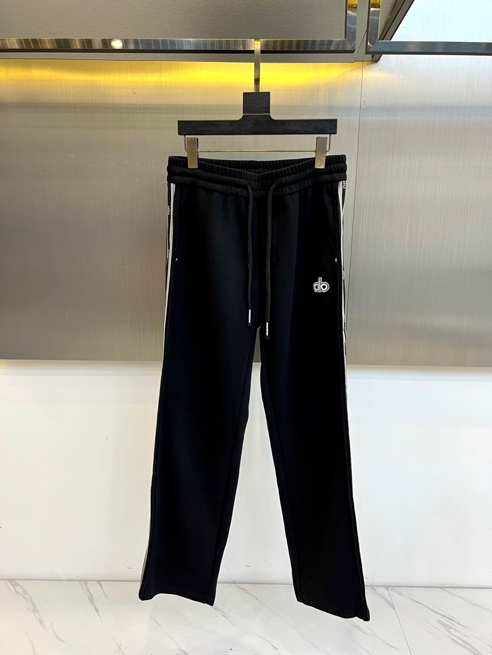 NO:529016,Alo's new 2025 autumn and winter thin velvet casual pants interpret the sports aesthetics with an iconic black tone. The elastic waist is built-in drawstring design to achieve a personalized fit experience with free adjustment. White stripes are decorated on both sides of the trouser body, extending from the waist to the trouser legs, forming a smooth visual line. The left leg is decorated with exquisite 'db' letter embroidered logo, highlighting the brand identity with three-dimensional needle method. It is made of high-performance thin velvet fabric, with fine fluff in the inner part providing warm care, and the outer layer maintains a neat and drape. The straight cut is combined with the design of micro-collapse trouser legs to take into account the freedom of movement and the urban fashion sense. The fabric is breathable and warm, adapting to the changing climate in autumn and winter.  The overall style perfectly combines sports functions and street fashion, and the black and white contrast design enhances the layering of the styling. You can use sports shoes to create a gym style, or casual boots to interpret the urban travel style. From morning jogging training to daily going out, you can interpret Alo's deep understanding of the aesthetics of sports life. The thin velvet inner ensures the comfortable body temperature of outdoor activities in autumn and winter, and becomes an all-round item with practicality and shape during the season transition period. It is recommended to wash and dry it in cold water to maintain the sharp contrast between the color of the black fabric and the white stripes. 48-56 (model 173, 143 catties upper body 50 sizes), boots, sneakers, alexander wang19860909Alo 2025秋冬新品薄绒休闲裤,以标志性黑色基调诠释运动美学.松紧腰头内置抽绳设计,实现自由调节的个性化贴合体验.裤身两侧饰有白色条纹,从腰际延伸至裤脚,形成流畅的视觉线条.左腿处点缀精致的「db」字母刺绣徽标,以立体针法凸显品牌身份. 采用高性能薄绒面料打造,内里细密绒毛提供温暖呵护,外层保持利落垂坠感.直筒剪裁配合微收裤脚设计,兼顾运动自由度与都市时尚感.面料兼具透气性与保暖性,适应秋冬多变气候. 整体风格完美融合运动功能与街头时尚,黑白对比设计增强造型层次感.既可搭配运动鞋打造健身房造型,亦可搭配休闲靴演绎都市出行风格.从晨跑训练到日常出街皆能胜任,诠释Alo对运动生活美学的深度理解.薄绒内里确保秋冬户外活动的舒适体温,成为季节过渡期兼具实用性与型格的全能单品.建议冷水手洗并平铺晾干,以保持黑色面料色泽与白色条纹的鲜明对比度.48-56（模特173,143斤上身50码）,,boots,sneakers,alexander wang,Men's clothing