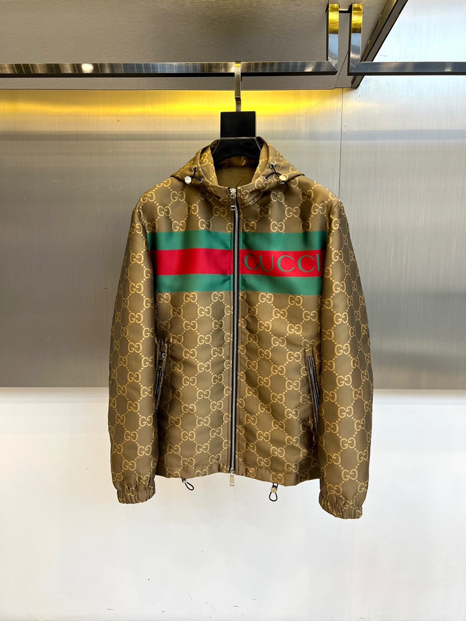 NO:529025,Gucc Gucci, the new autumn and winter jacket of 2025, is based on dark brown, and the fabric is covered with the brand's iconic gold double G pattern, highlighting the rich retro and luxurious atmosphere. In terms of style design, the hooded shape is matched with smooth zipper opening and closing, taking into account practicality and modernity; the eye-catching green and red webbing stripes on the chest run through the left and right, with black GUCCI printed on it, instantly improving visual recognition; zipper pockets are set on both sides to cleverly blend functionality and overall design language. The tailoring is neat and the silhouette is focused on giving the wearer an elegant and confident figure. In terms of style, this jacket perfectly interprets Gucci's fusion of retro aesthetics  With the genes of contemporary fashion, the collision of double G patterns and green and red stripes is both classic and bold, and the dark brown background is calm and high-end, suitable for creating a variety of styles - whether it is matched with simple inner wear to highlight the item itself, or combined with the same series of bottoms to enhance the overall feeling, it can show impeccable taste in autumn and winter occasions. It is not only a warm and practical item, but also a fashion statement that highlights Italian luxury and street aristocratic atmosphere, suitable for fashion enthusiasts who pursue the ultimate style and brand loyalty. 48-56 (model 173, 143 catties upper body 50 sizes), gucci, gucci, jackets  & coats,hats,alexander wang19860909Gucc古驰、2025秋冬新品夹克,以深棕色为基调,面料上铺满品牌标志性的金色双G图案,彰显浓郁复古奢华气息.款式设计上,连帽造型搭配顺滑拉链开合,兼顾实用性与现代感；胸前醒目的绿红织带条纹贯穿左右,其上印有黑色GUCCI字样,瞬间提升视觉辨识度；两侧设拉链口袋,巧妙融合功能性与整体设计语言.剪裁利落且注重廓形,赋予穿着者优雅而自信的体态.风格上,这款夹克完美诠释了古驰融合复古美学与当代时尚的基因,双G图案与绿红条纹的碰撞既经典又大胆,深棕底色沉稳高级,适合打造多种造型——无论是搭配简约内搭突出单品本身,或与同系列下装组合强化整体感,都能在秋冬场合中展现无可挑剔的品味.它不仅是保暖实用单品,更是彰显意式奢华与街头贵族气息的时尚宣言,适合追求极致风格与品牌忠诚度的时尚爱好者.48-56（模特173,143斤上身50码）,,gucci,gucci,jackets & coats,hats,alexander wang,Men's clothing