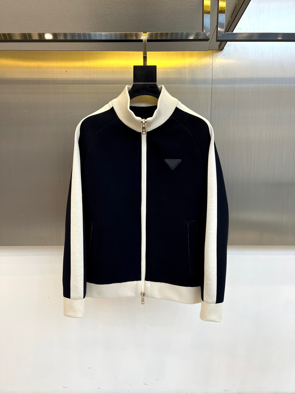 NO:529032,Prada, 2025 autumn and winter new jacket, interprets Italian luxury new style with classic contrasting color design. The three-dimensional tailored baseball collar design is matched with a crisp silhouette, using black textured high-tech fabric and white ribbed trim to form a sharp visual contrast. The front closure is equipped with an iconic silver metal zipper, embellished with three-dimensional triangle enamel badges, highlighting the brand genes in the details. The cuffs use double-layer ribbed edges to enhance the sports aesthetics, and the double-sided oblique pockets take into account practical functions and styling levels. The style perfectly combines retro sports elements and high-end  Fashion language, the cold color combination of matte black and pearl white bursts out a futuristic modern atmosphere, which not only retains the brand's consistent minimalist aesthetics, but also shows the exquisite style of contemporary urban elites through material collision and structural lines. This jacket can not only show the creativity of mixing and matching, but also match casual items to highlight low-key luxury, becoming an iconic item in autumn and winter wardrobe that has both practicality and brand recognition. 48-56 (model 173, 143 catties upper body 50 sizes),, prada, prada, jackets  & coats,alexander wang19860909Prada普拉、2025秋冬新品夹克,以经典撞色设计诠释意式奢华新风尚.立体剪裁的棒球领设计搭配挺括廓形,采用黑色肌理感高科技面料与白色罗纹饰边形成鲜明视觉对比.前襟配备标志性银色金属拉链,点缀立体三角形珐琅徽章,细节处彰显品牌基因.袖口采用双层罗纹收边强化运动美学,双侧斜插口袋兼顾实用功能与造型层次.风格上完美融合复古运动元素与高级时装语言,哑光黑与珍珠白的冷调配色迸发出未来感摩登气息,既保留品牌一贯的极简主义美学,又通过材质碰撞和结构线条展现当代都会精英的精致格调.这款夹克既能搭配正装展现混搭创意,亦可搭配休闲单品凸显低调奢华,成为秋冬衣橱中兼具实用性与品牌辨识度的标志性单品.48-56（模特173,143斤上身50码）,,prada,prada,jackets & coats,alexander wang,Men's clothing