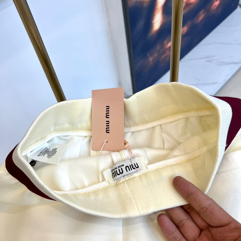 Miu Miu 2025秋冬新品米白色休闲裤，以纯净色调演绎现代少女式叛逆。腰头处饰有酒红色镶边撞色设计