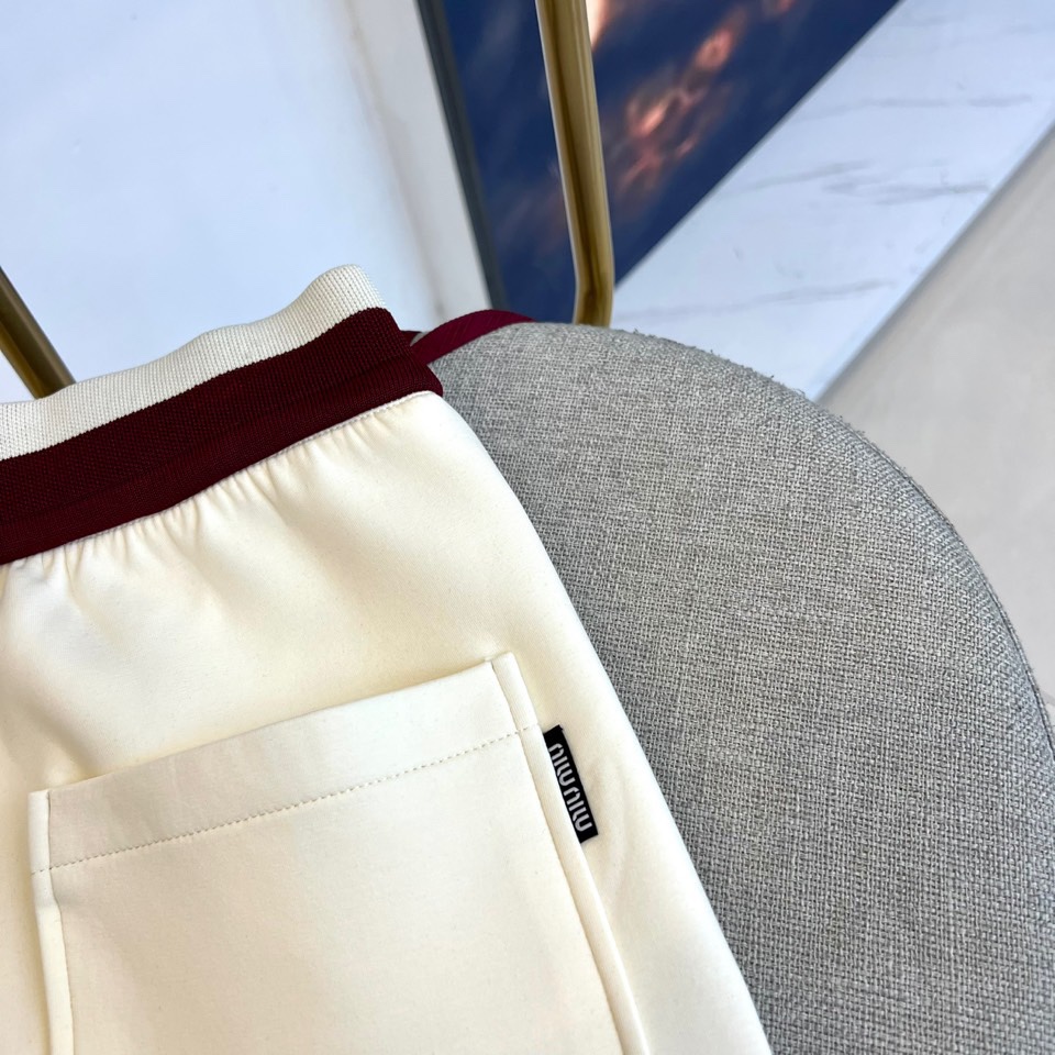 Miu Miu 2025秋冬新品米白色休闲裤，以纯净色调演绎现代少女式叛逆。腰头处饰有酒红色镶边撞色设计