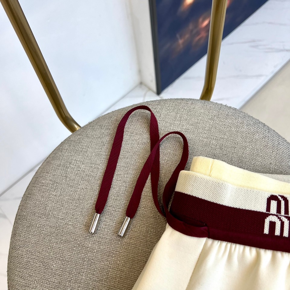 Miu Miu 2025秋冬新品米白色休闲裤，以纯净色调演绎现代少女式叛逆。腰头处饰有酒红色镶边撞色设计