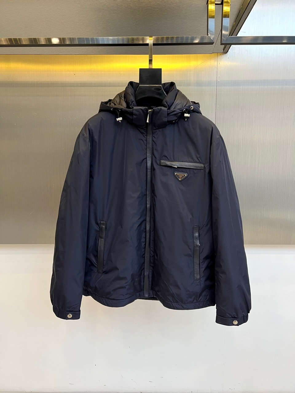 NO:539030,Prada, the new down jacket for autumn and winter 2025, interprets modern minimalist aesthetics in classic black. This down jacket is made of polyamide fabric, combining excellent warmth and light texture. The hooded design is paired with a smooth zipper opening and closing system, and the left chest is decorated with the brand's iconic triangular logo, showing a low-key and luxurious identity. Both sides are equipped with practical pockets with zippers, with leather edges embellished with details, and metal snaps on the cuffs for elastic adjustment. Slim-fitting cut  Clever and clever, the down filling is evenly distributed to ensure warmth. The practical functions are integrated with high-end fashion language, so that the detailed craftsmanship becomes a quality declaration for winter outfits. It can not only create a modern urban image with formal wear, but also collide with casual wear to create a mixed-match charm, perfectly interpreting Prada's in-depth exploration of the balance of functionality and aesthetics. 48-56 (model 173, 143 catties upper body 50 yards),,prada,prada,down  Jacket, Hats, Alexander wang19860909Prada普拉、2025秋冬新品羽绒服,以经典黑色演绎现代极简美学.这款羽绒服采用聚酰胺面料打造,兼具出色保暖性能与轻盈质感.连帽设计搭配顺滑拉链开合系统,左胸饰有品牌标志性三角徽标,彰显低调奢华身份.两侧配备带拉链的实用口袋,边缘以皮质镶边点缀细节,袖口设金属按扣实现松紧调节.修身剪裁利落挺括,羽绒填充均匀分布确保保暖性.将实用功能与高级时装语言相融合,让细节工艺成为冬日穿搭的品质宣言.既可搭配正装塑造都市摩登形象,也能与休闲装碰撞出混搭魅力,完美诠释Prada对功能性与美学平衡的深度探索.48-56（模特173,143斤上身50码）,,prada,prada,down jacket,hats,alexander wang,Men's clothing