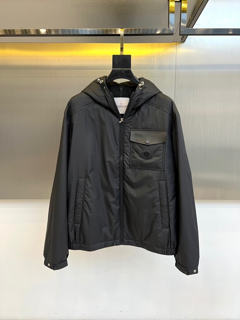 Mon蒙口、2025秋冬新品 男士连帽棉服夹克外套。这款黑色夹克采用立领连帽设计,帽檐与前襟配备银色金属