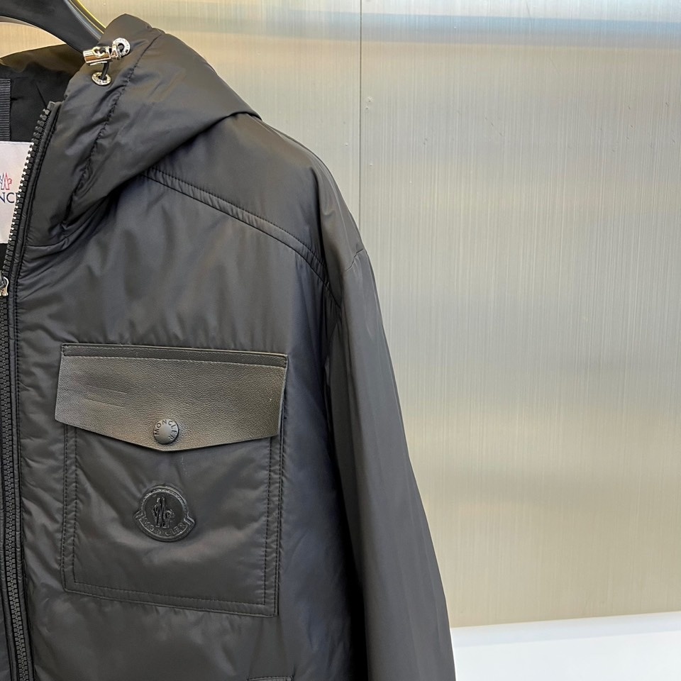 Mon蒙口、2025秋冬新品 男士连帽棉服夹克外套。这款黑色夹克采用立领连帽设计,帽檐与前襟配备银色金属